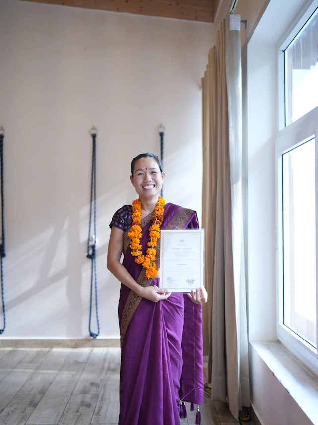 A woman in a sari holds a certificate indoors.