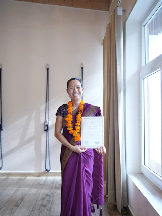 A woman in a sari holds a certificate indoors.