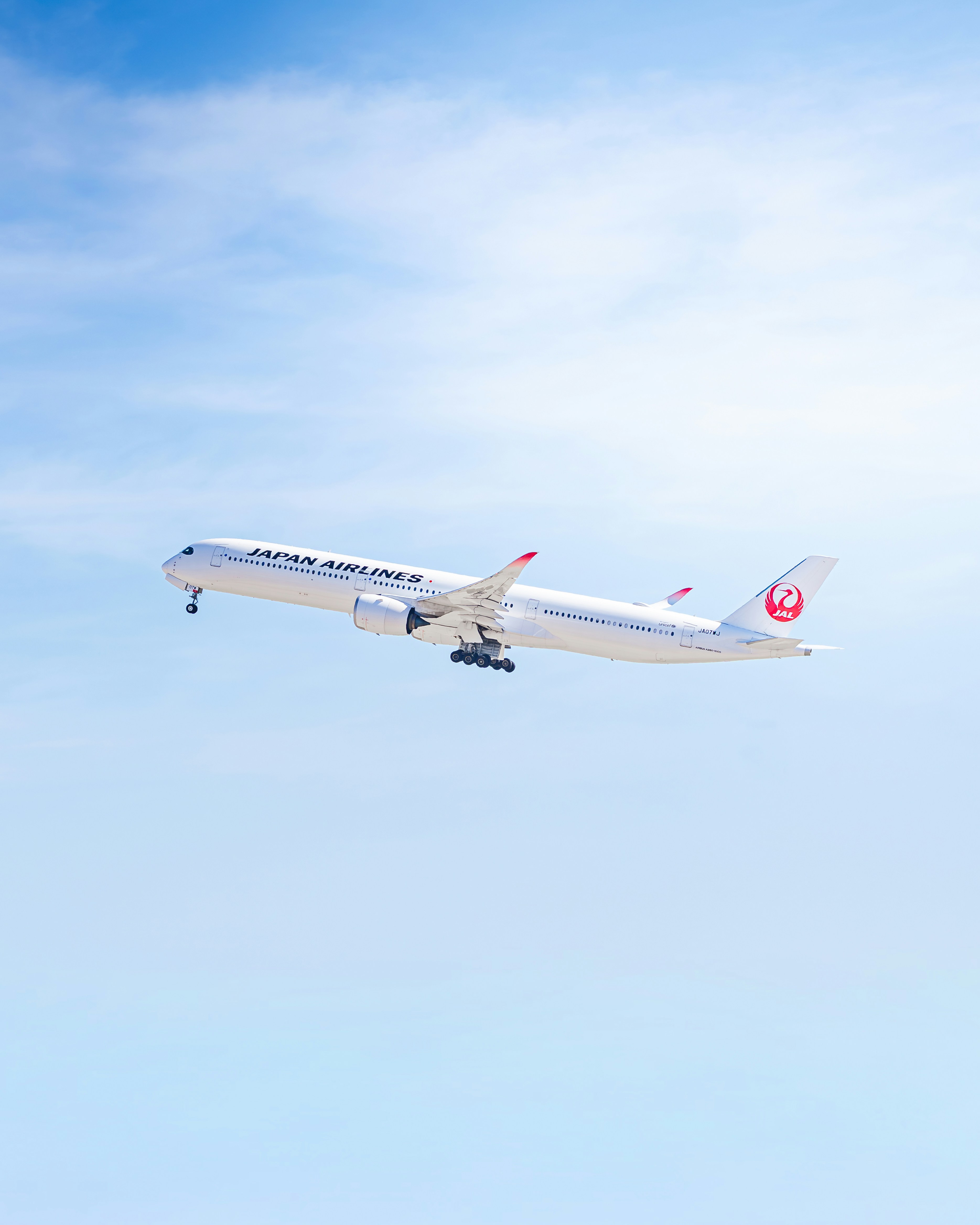 A japan airlines airplane ascends into a clear blue sky.