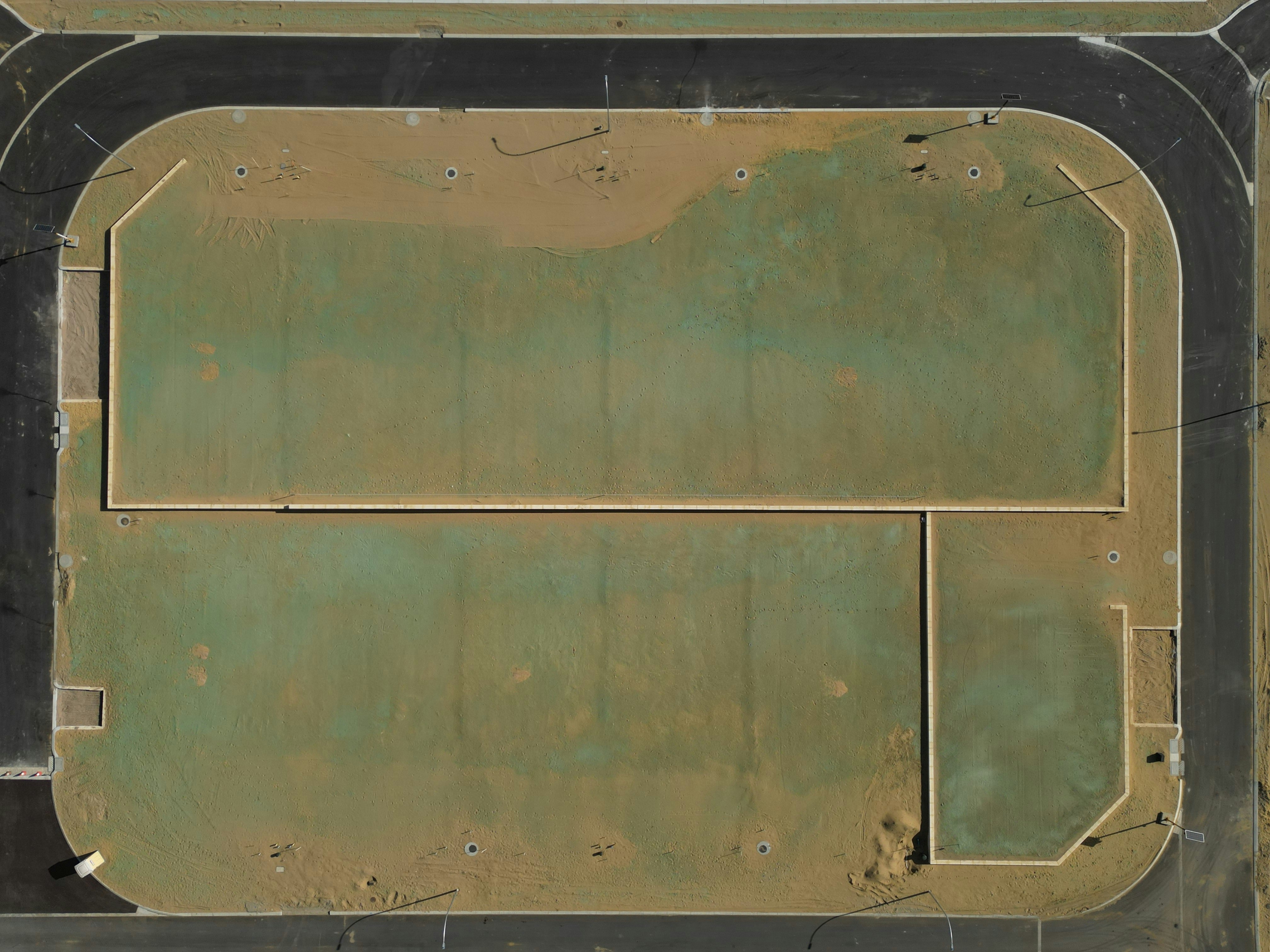 Vue aérienne d’un terrain sportif poussiéreux et vert.