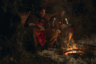 Two medieval warriors resting by a campfire at night.