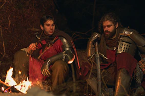 Two knights in armor resting by a campfire