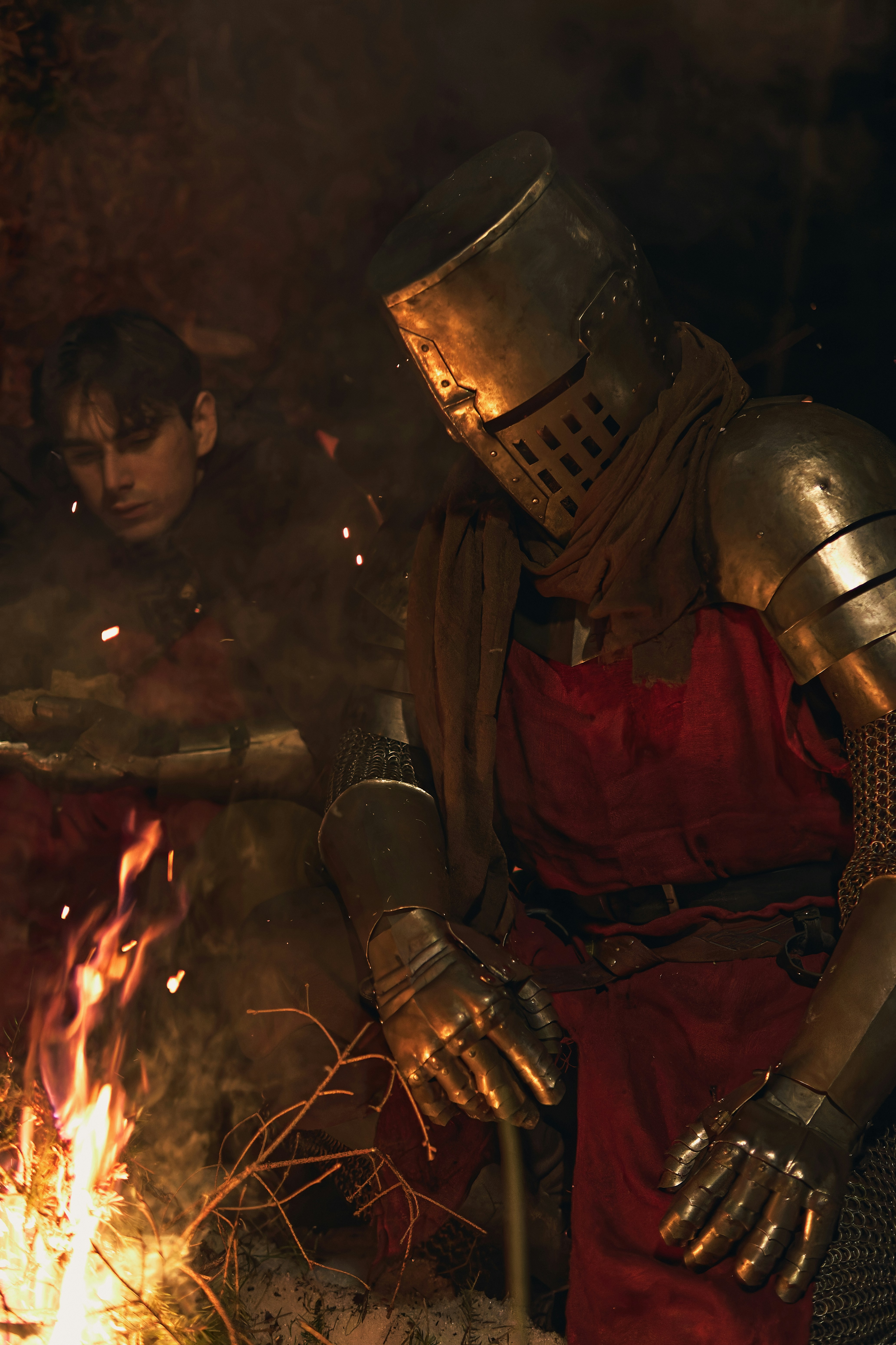 Knight in armor by a campfire with another person
