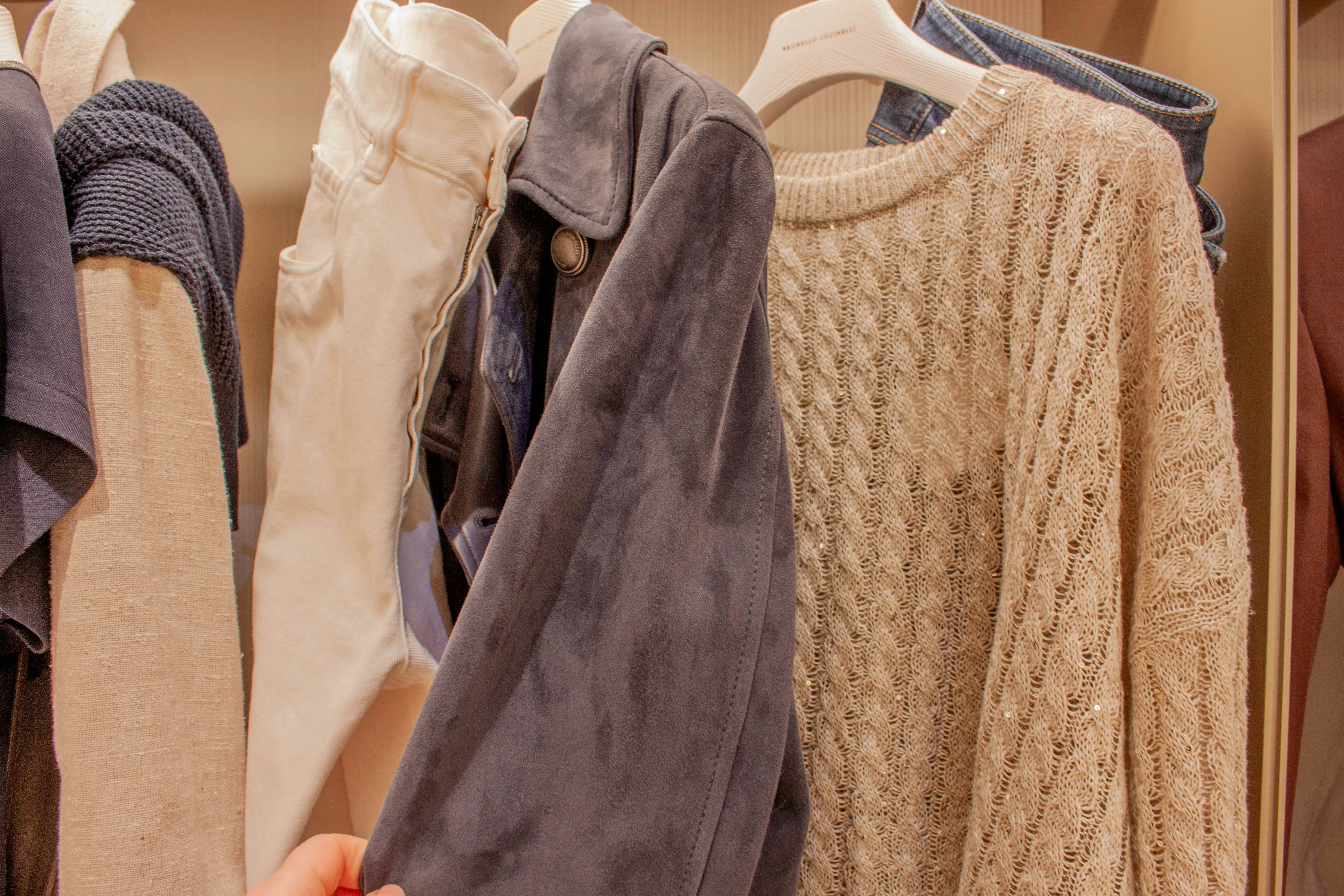 A hand reaches for a gray jacket in a closet.