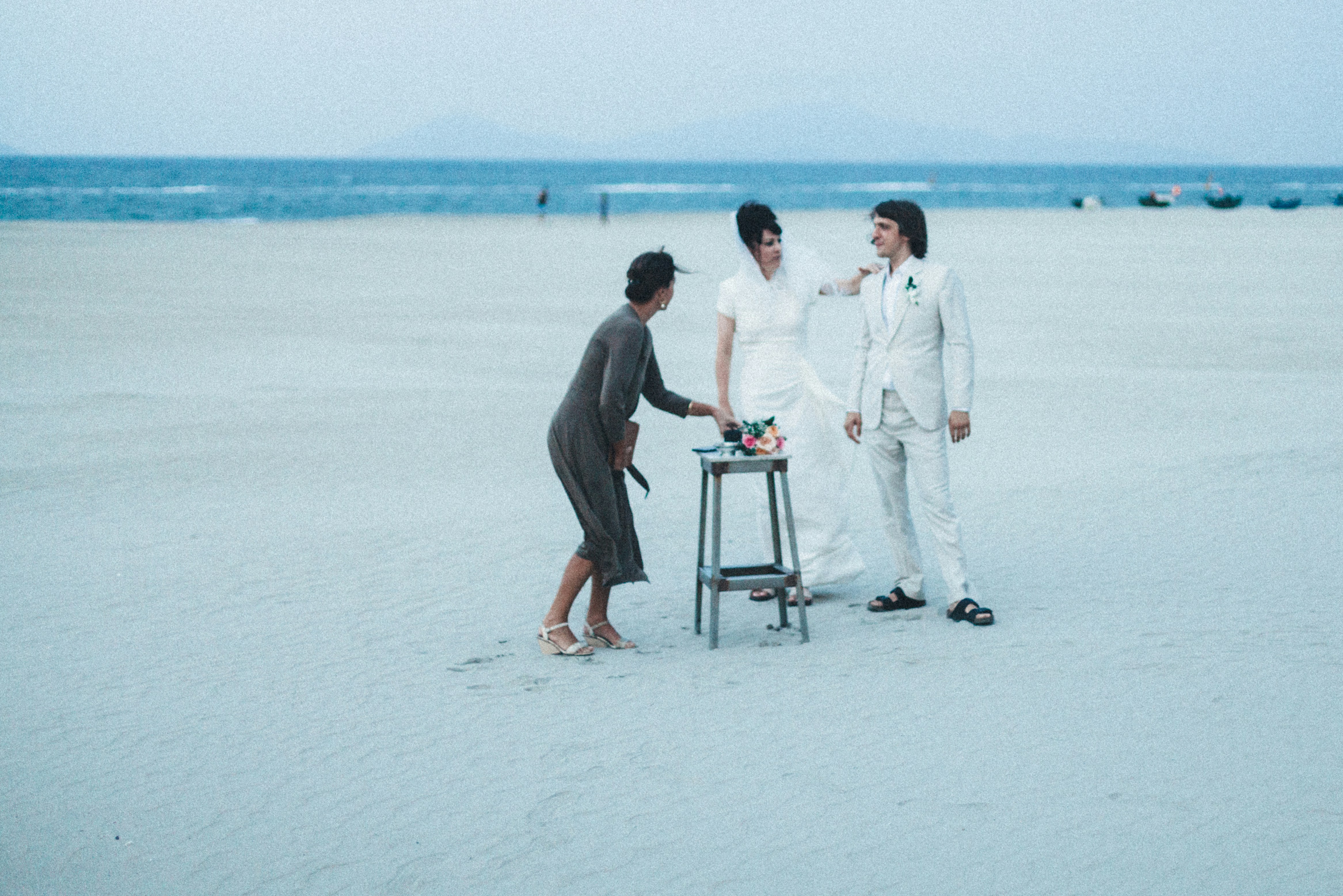 Three people gathered on a sandy beach by the ocean.