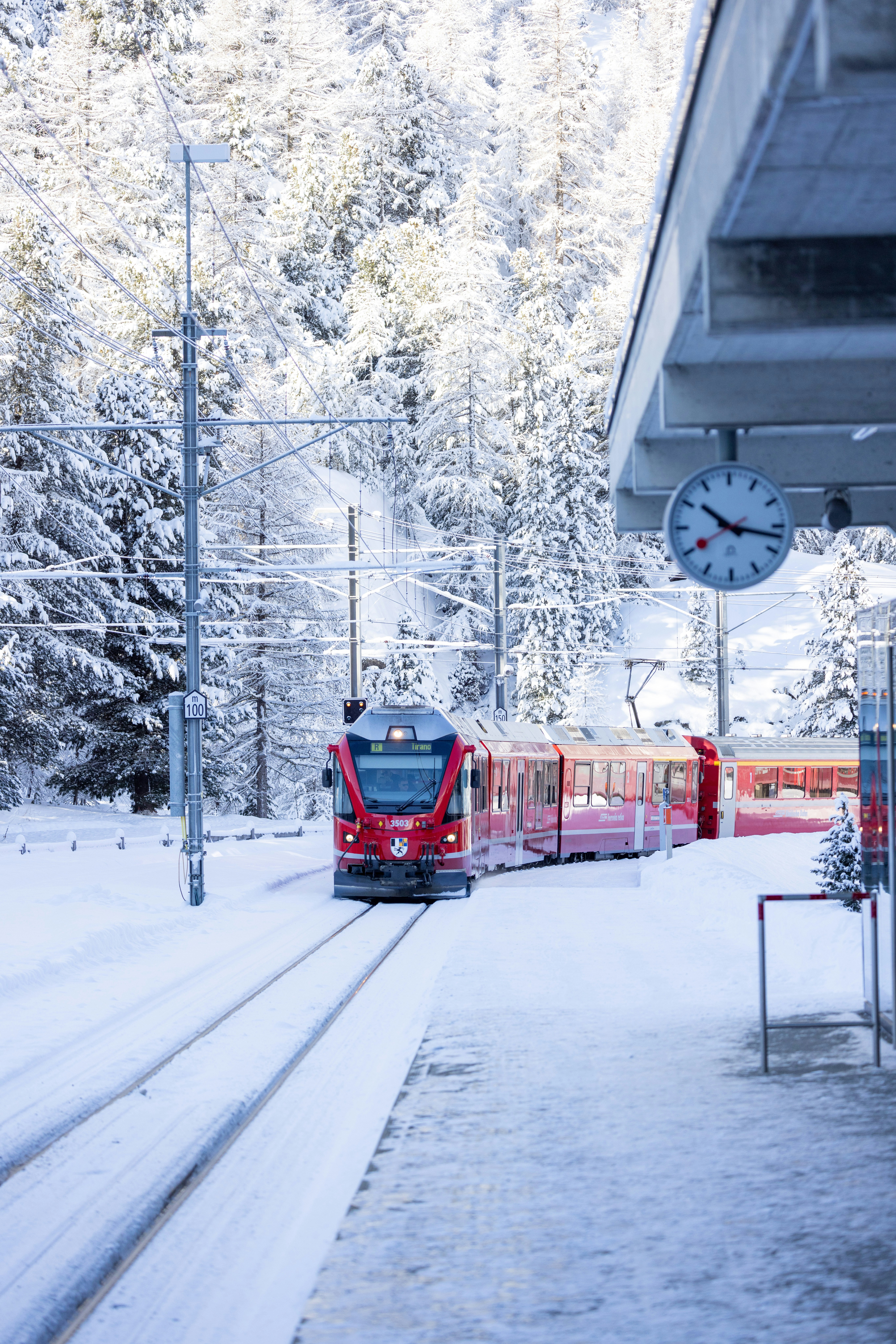 A red train waits at a snowy station platform.