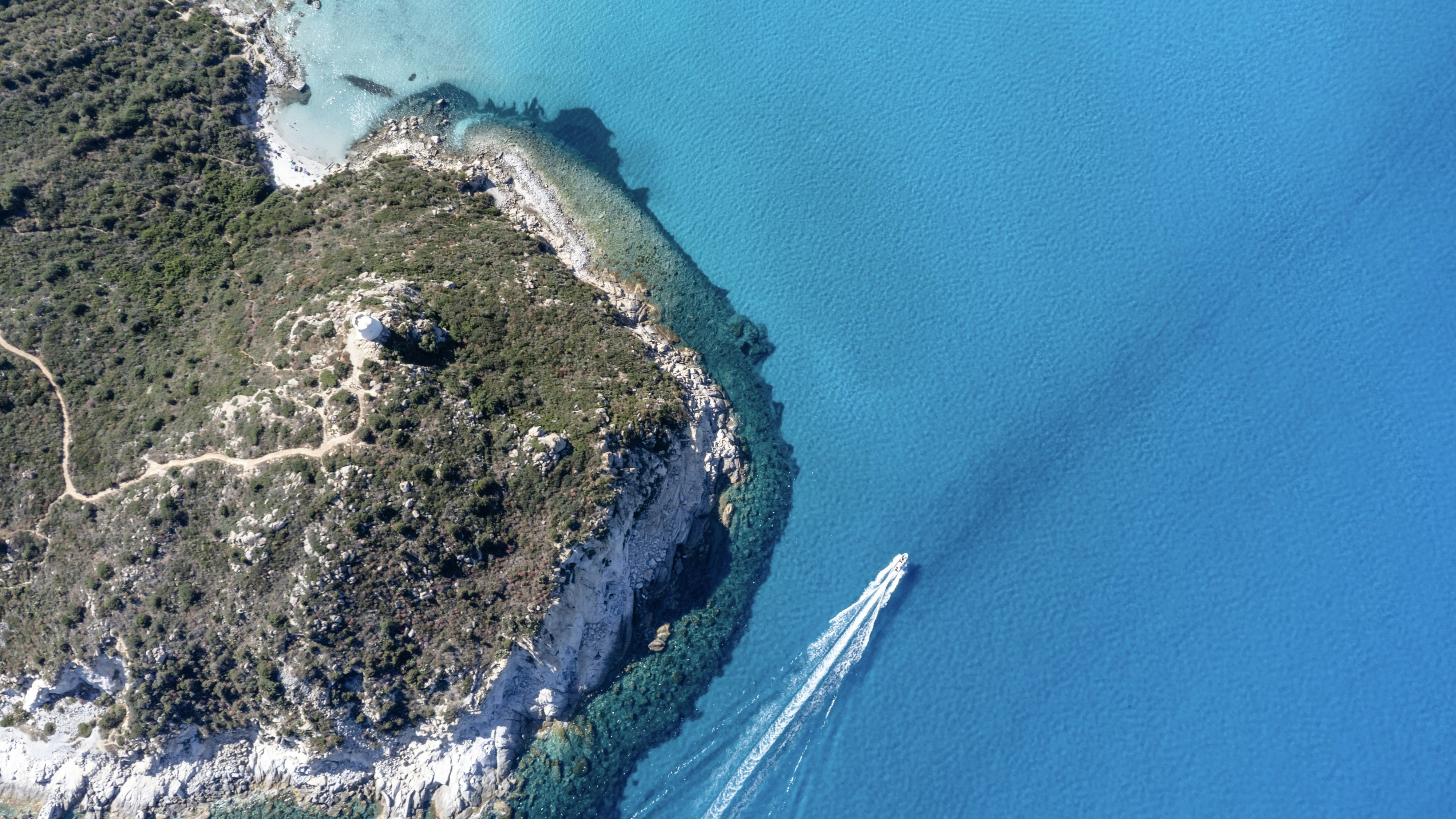 Boat sailing on bright blue ocean near rocky coast
