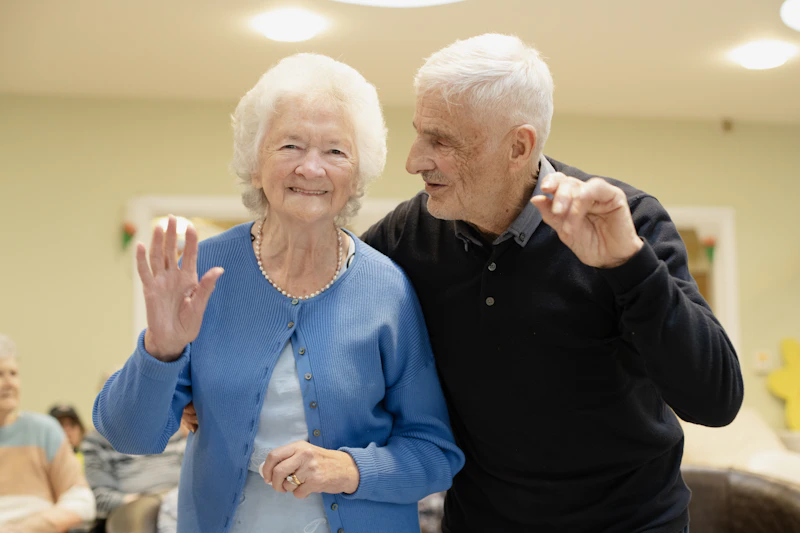 elderly couple warmly waving hello indoors
