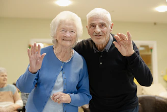 Elderly couple waving and smiling at the camera.