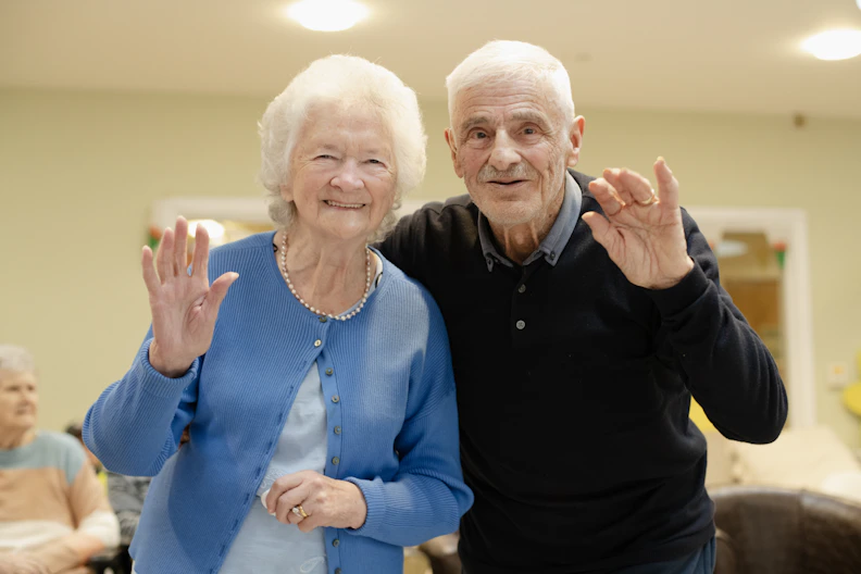 Elderly couple waving and smiling at the camera.