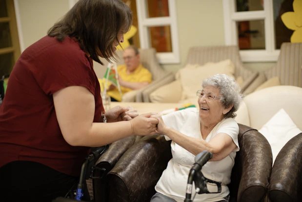 Caregiver assists elderly woman with walker.