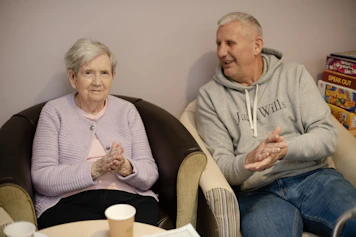 Elderly woman and man sitting in chairs clapping.
