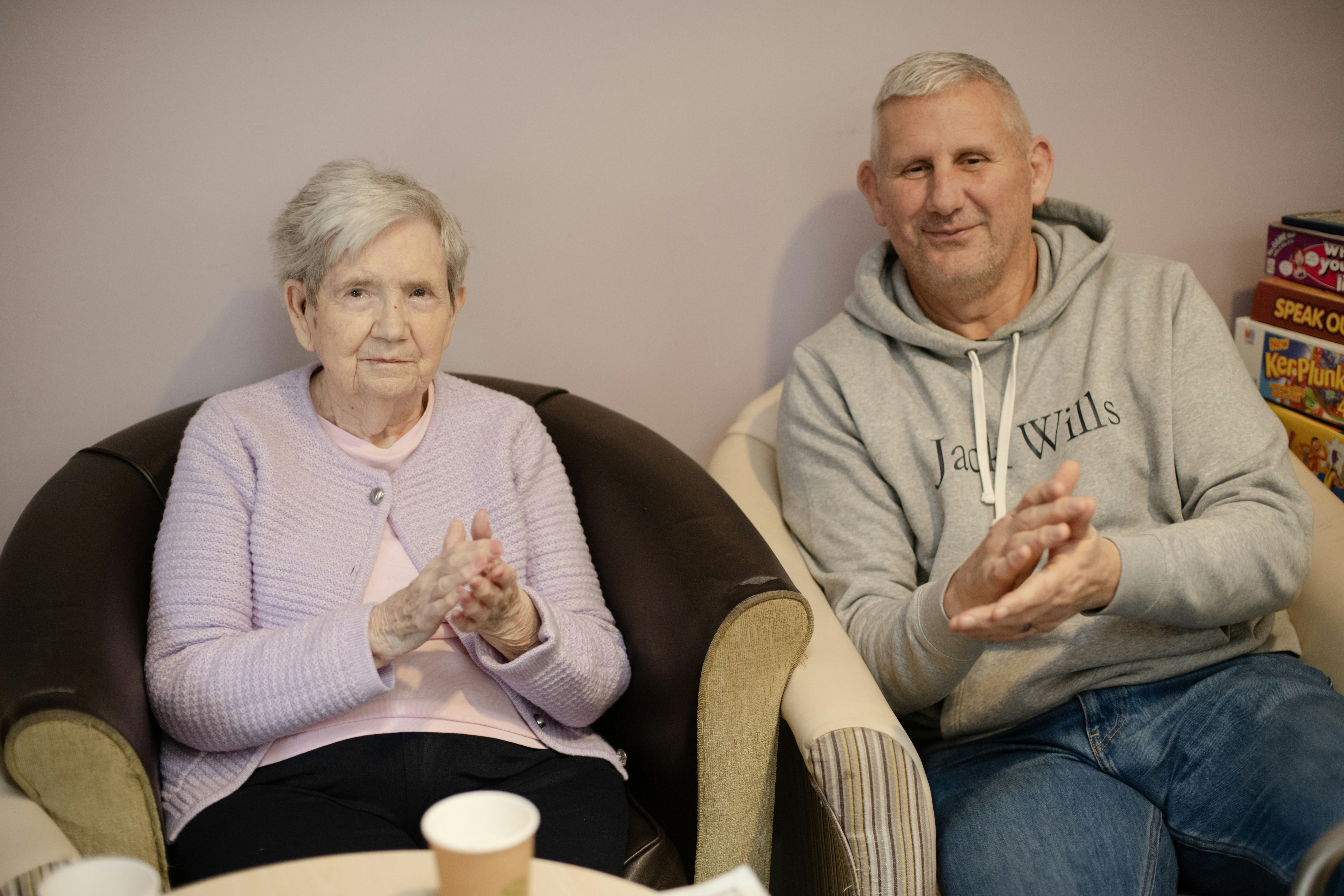 Elderly woman and man clapping in chairs.