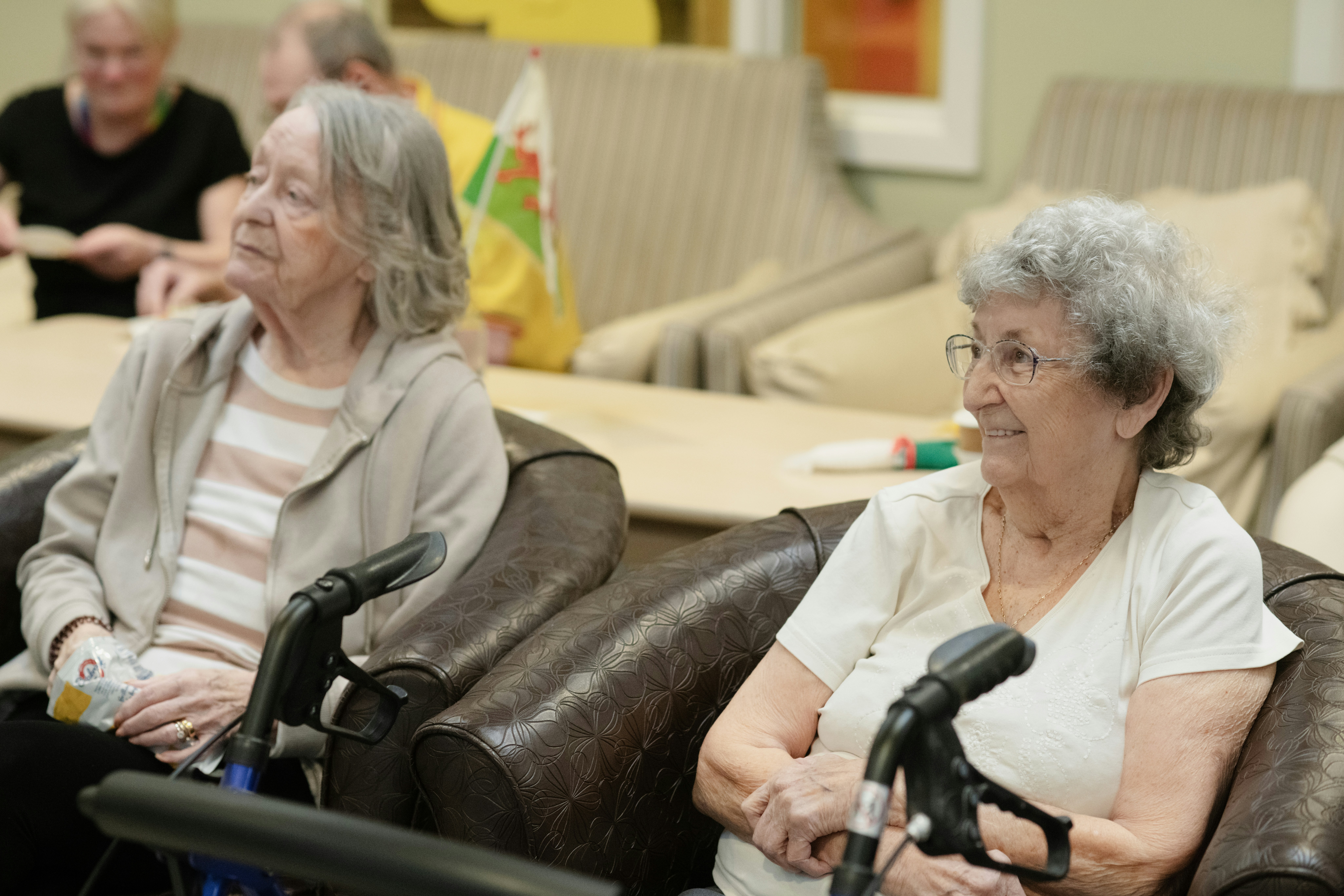 Two elderly women sitting in chairs at a gathering.