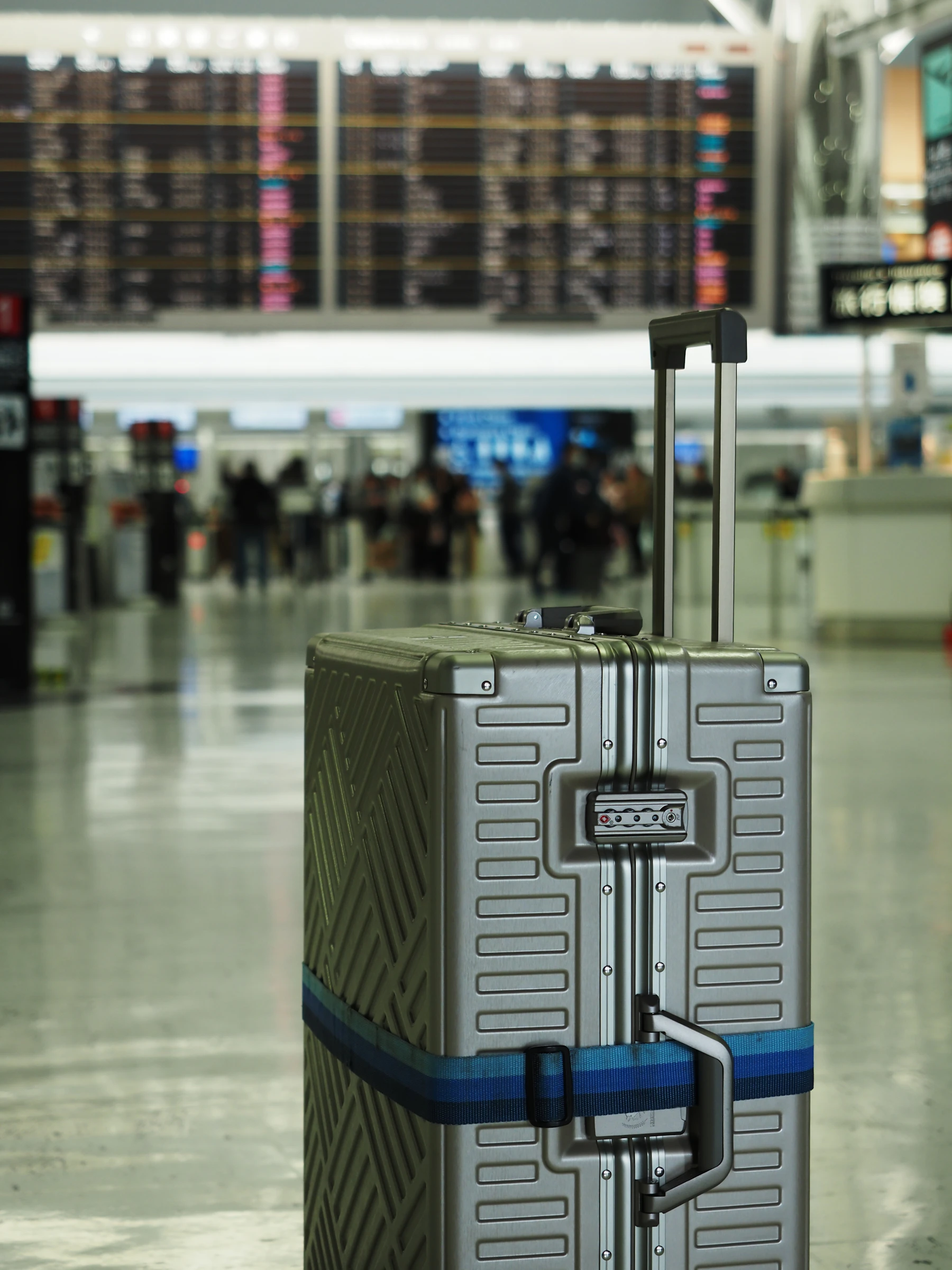 Silver hard-shell carry-on suitcase waiting in an airport terminal