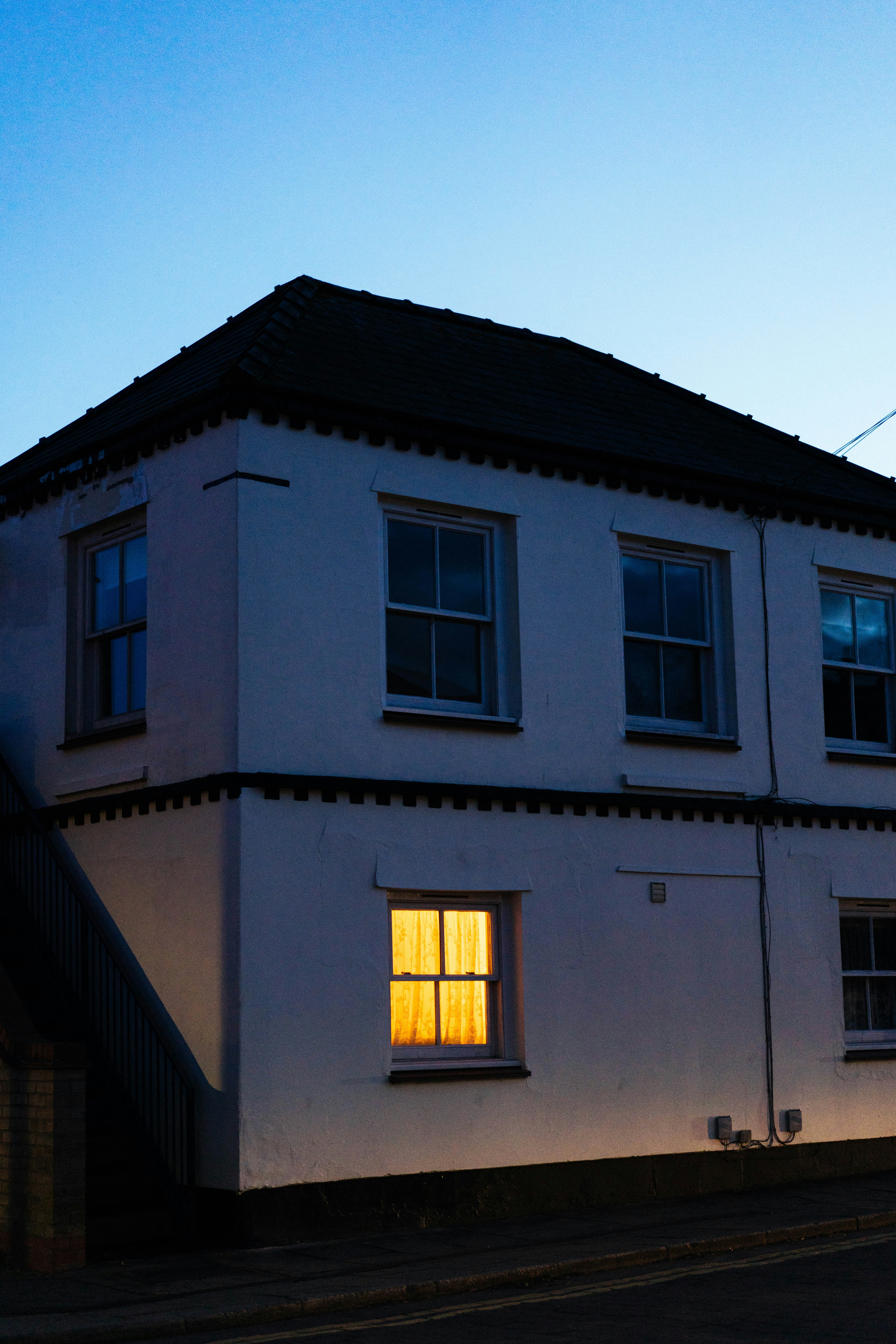 A white building with one illuminated window at dusk.