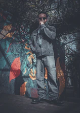 Man in denim jacket and jeans stands near mural