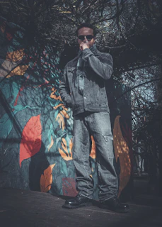 Man in denim jacket and jeans stands near mural