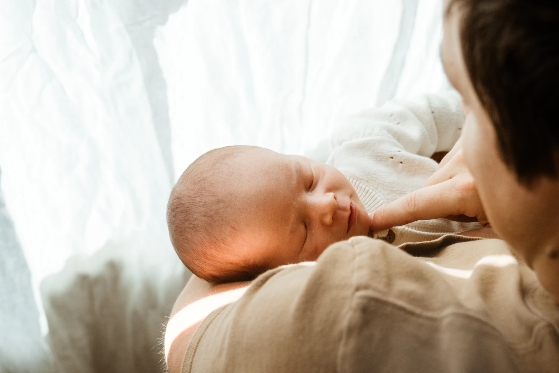 Parent gently holding a peaceful sleeping newborn near a bright window