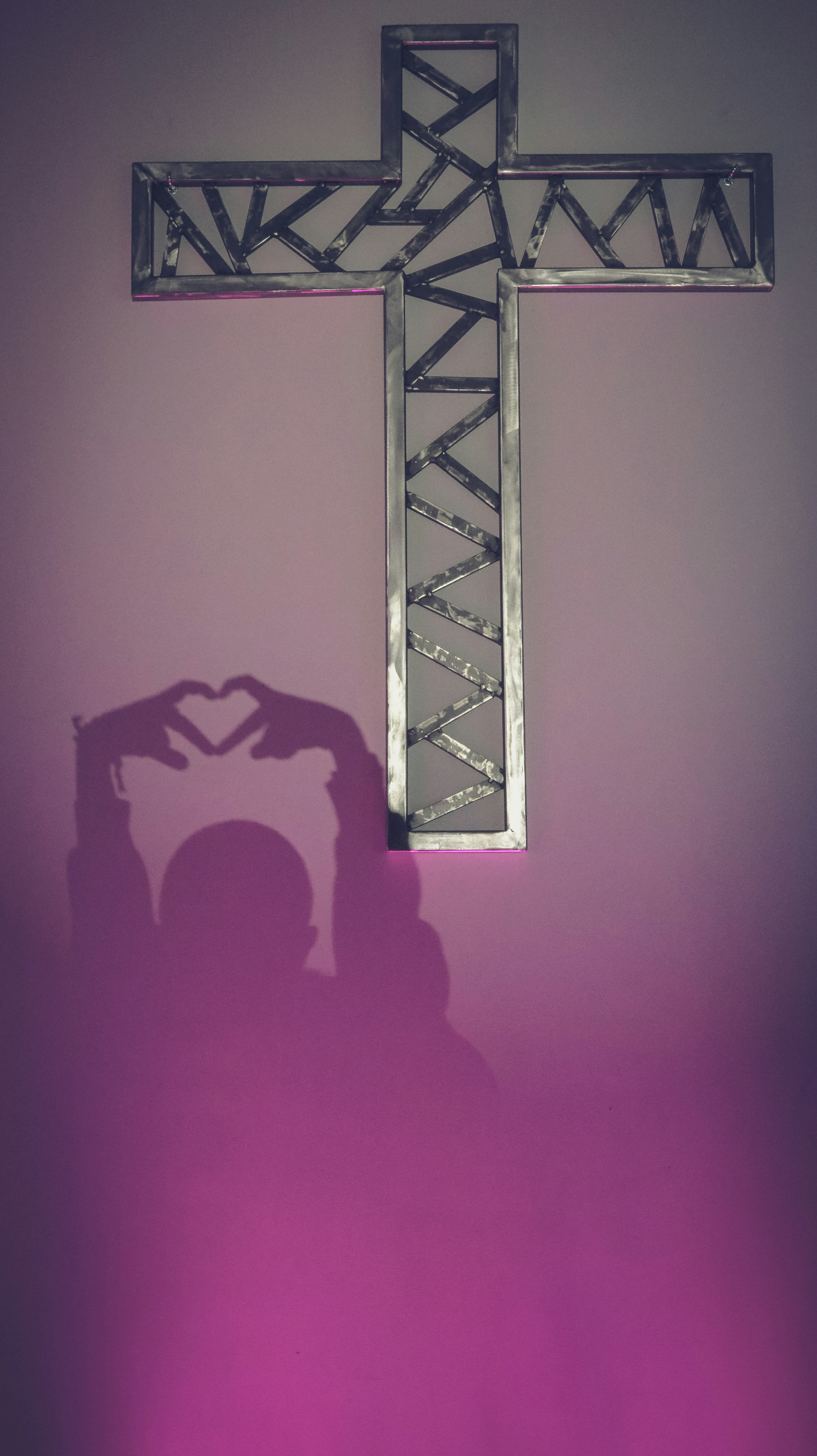 Shadow of a person making heart shape near a cross