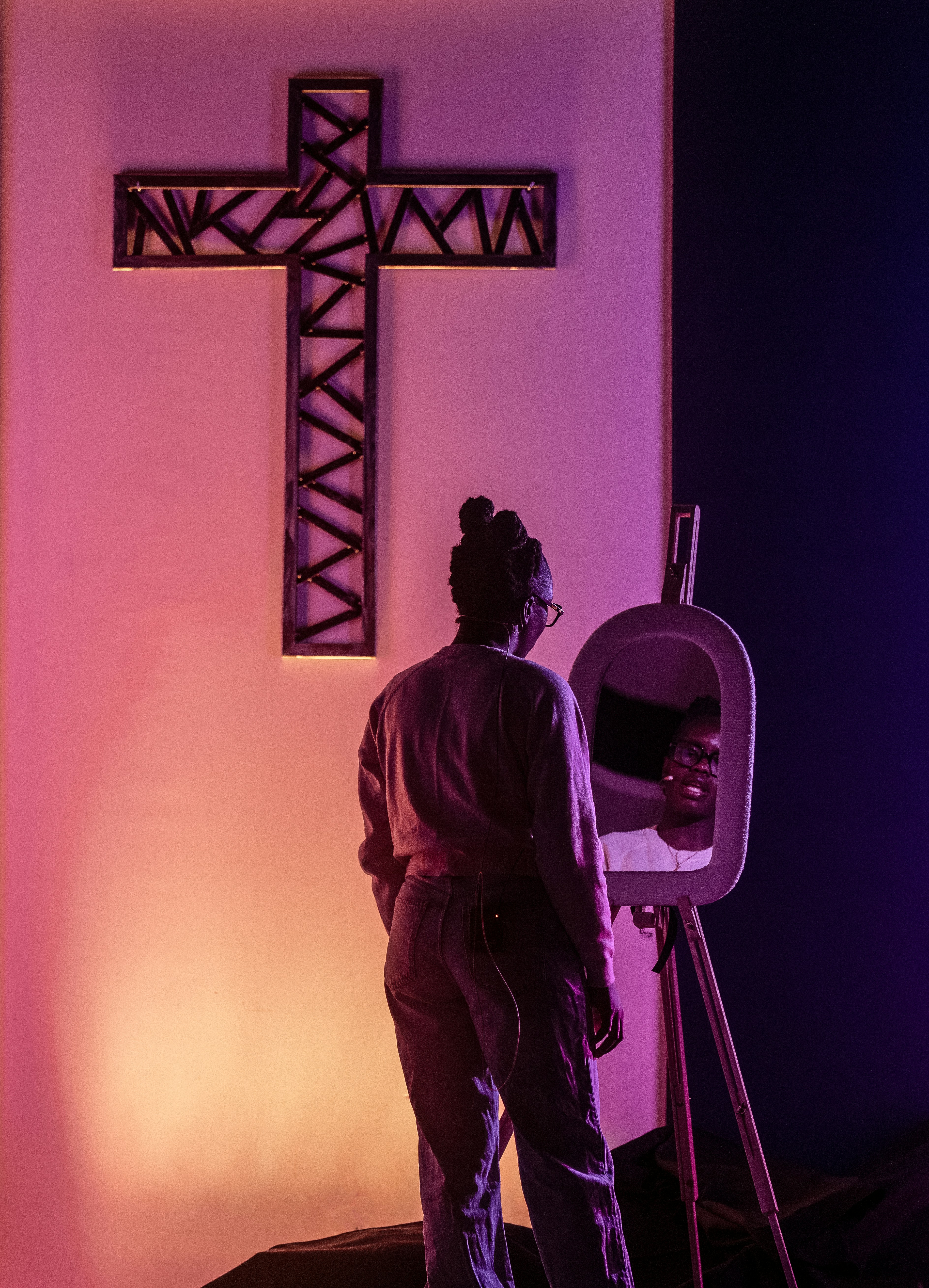 Frau blickt in den Spiegel nahe dem beleuchteten Kreuz