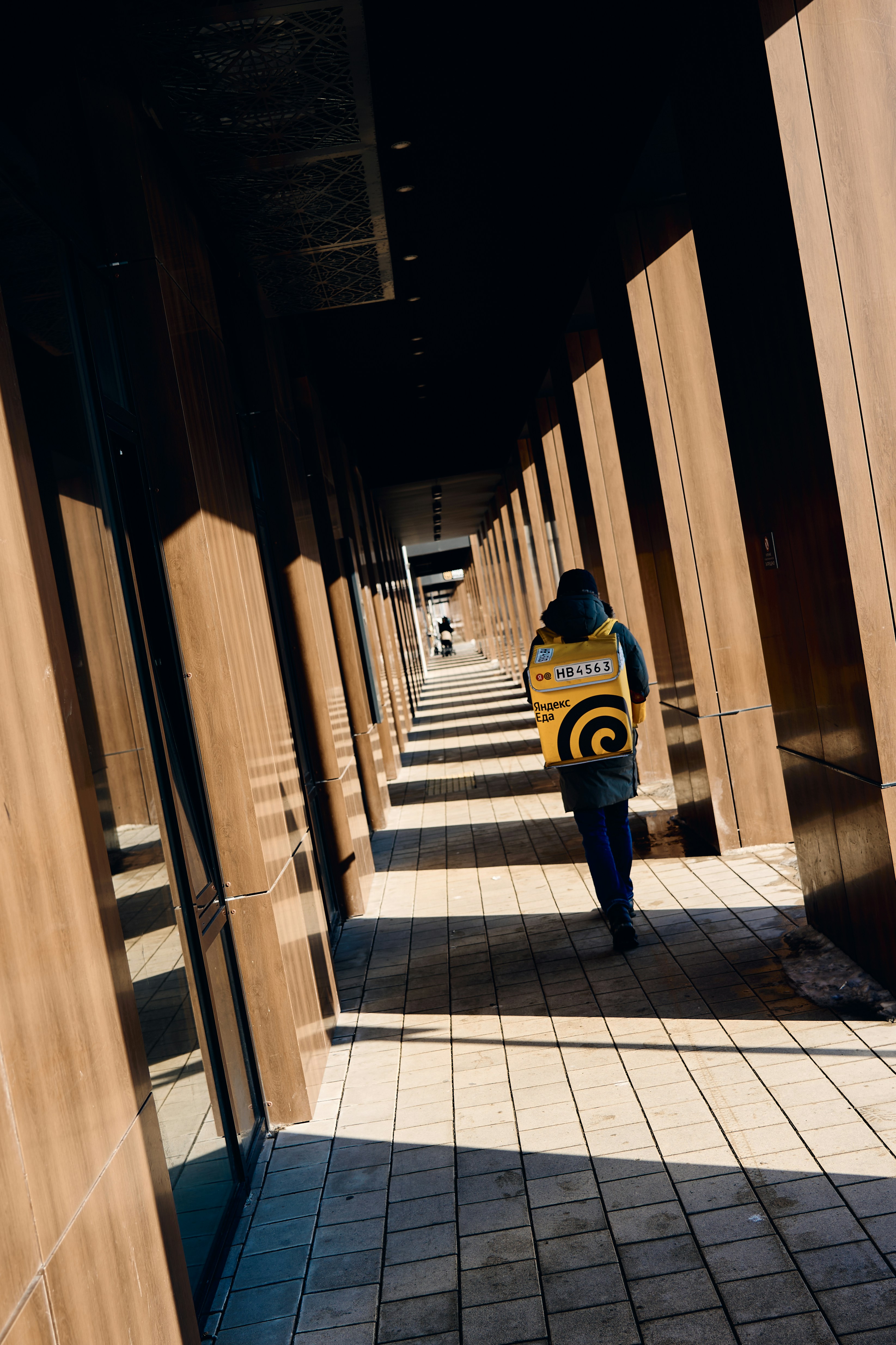Person with yellow delivery bag walks down sunlit corridor.