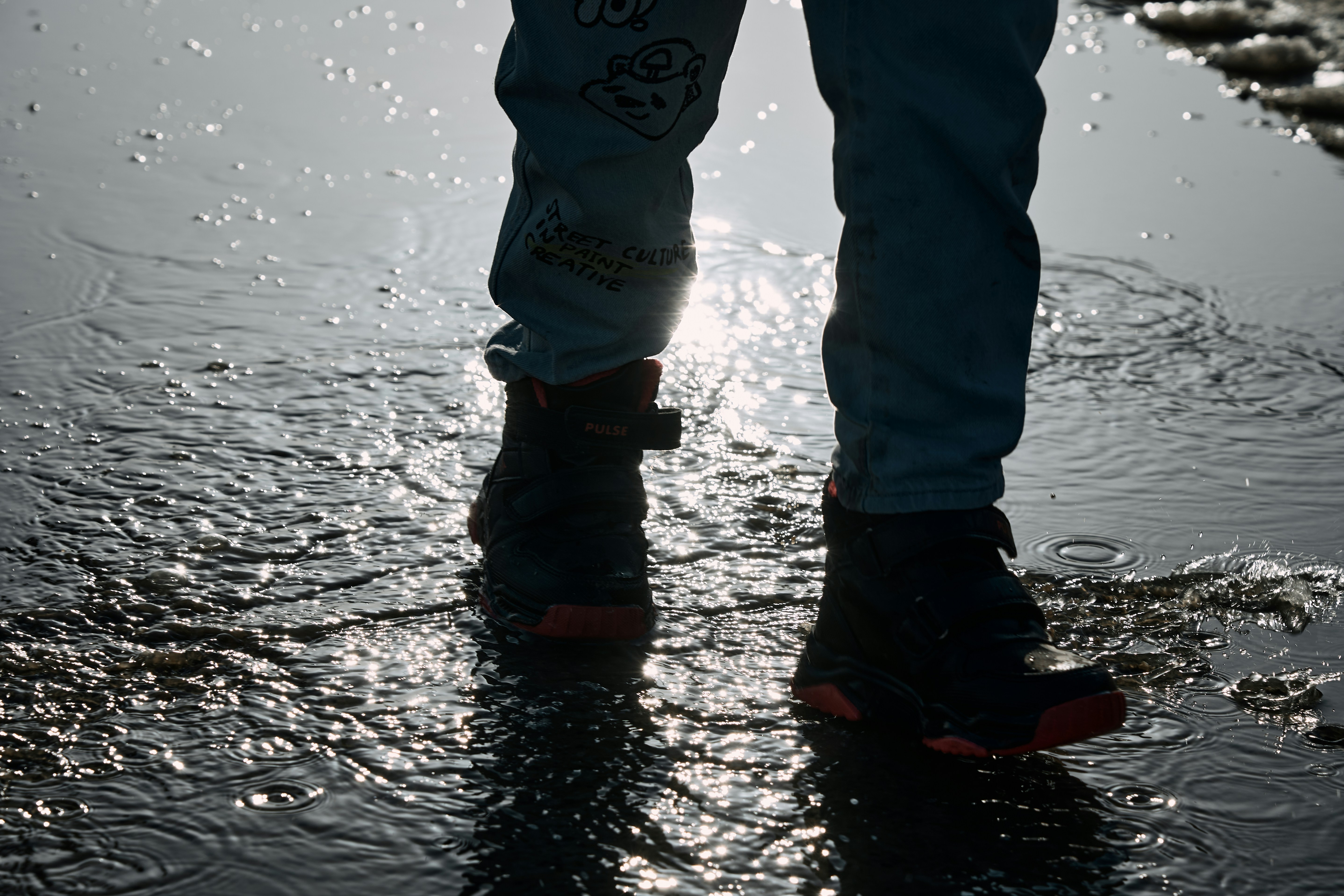 Child in boots splashing in shallow water