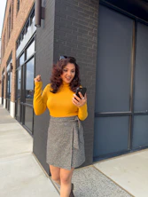 Woman in yellow top and skirt looking at phone.