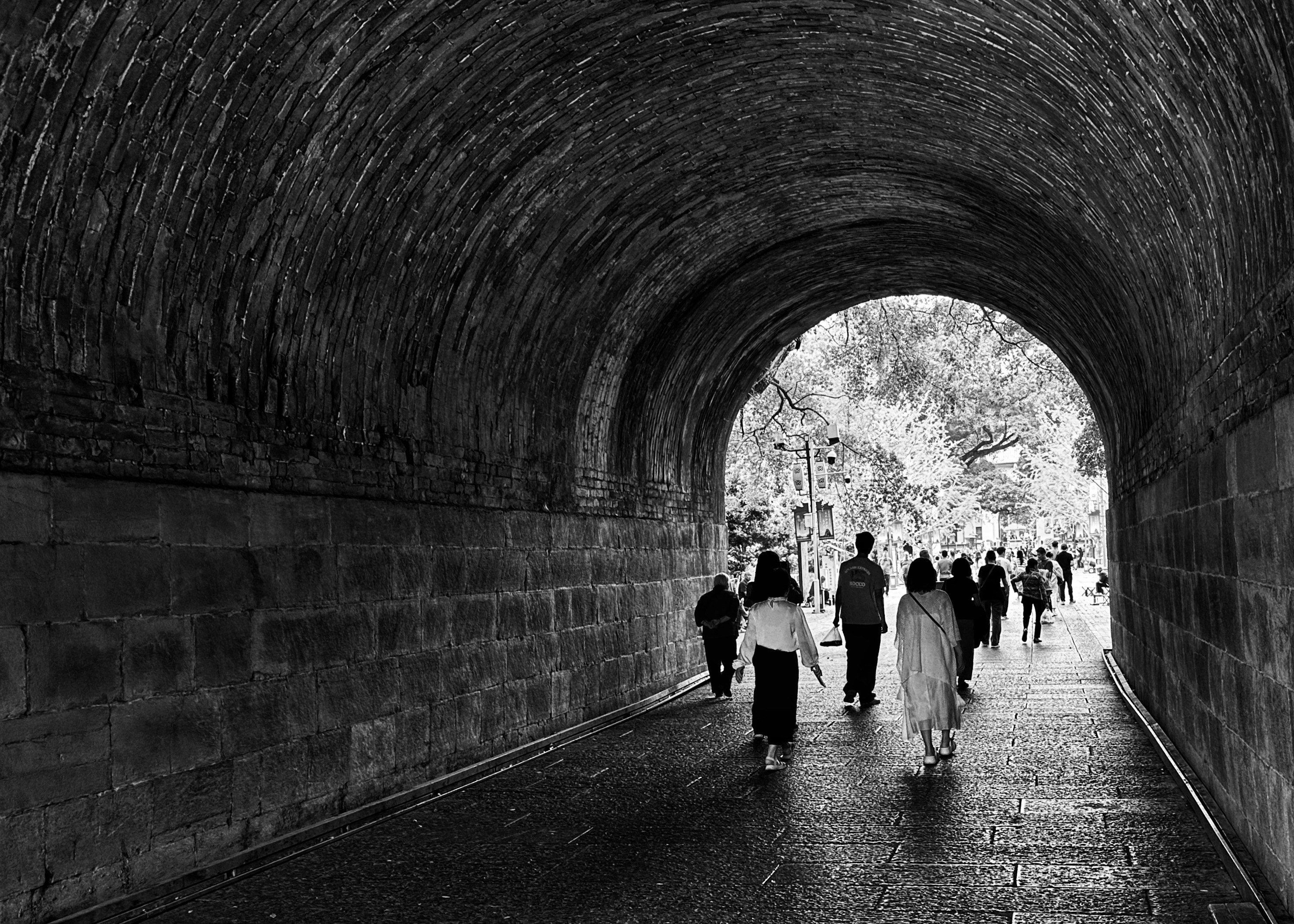 People walk through a stone tunnel towards daylight.