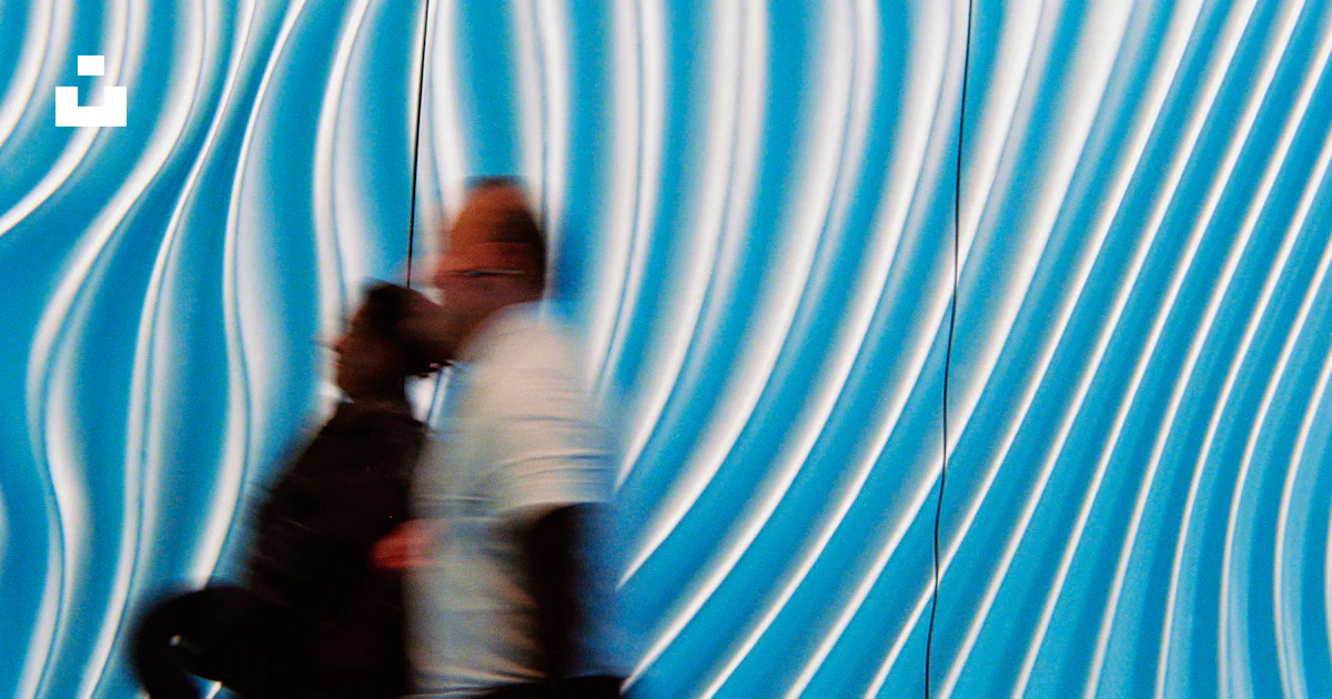 Two people walking past a blue and white wavy wall photo – Free ...