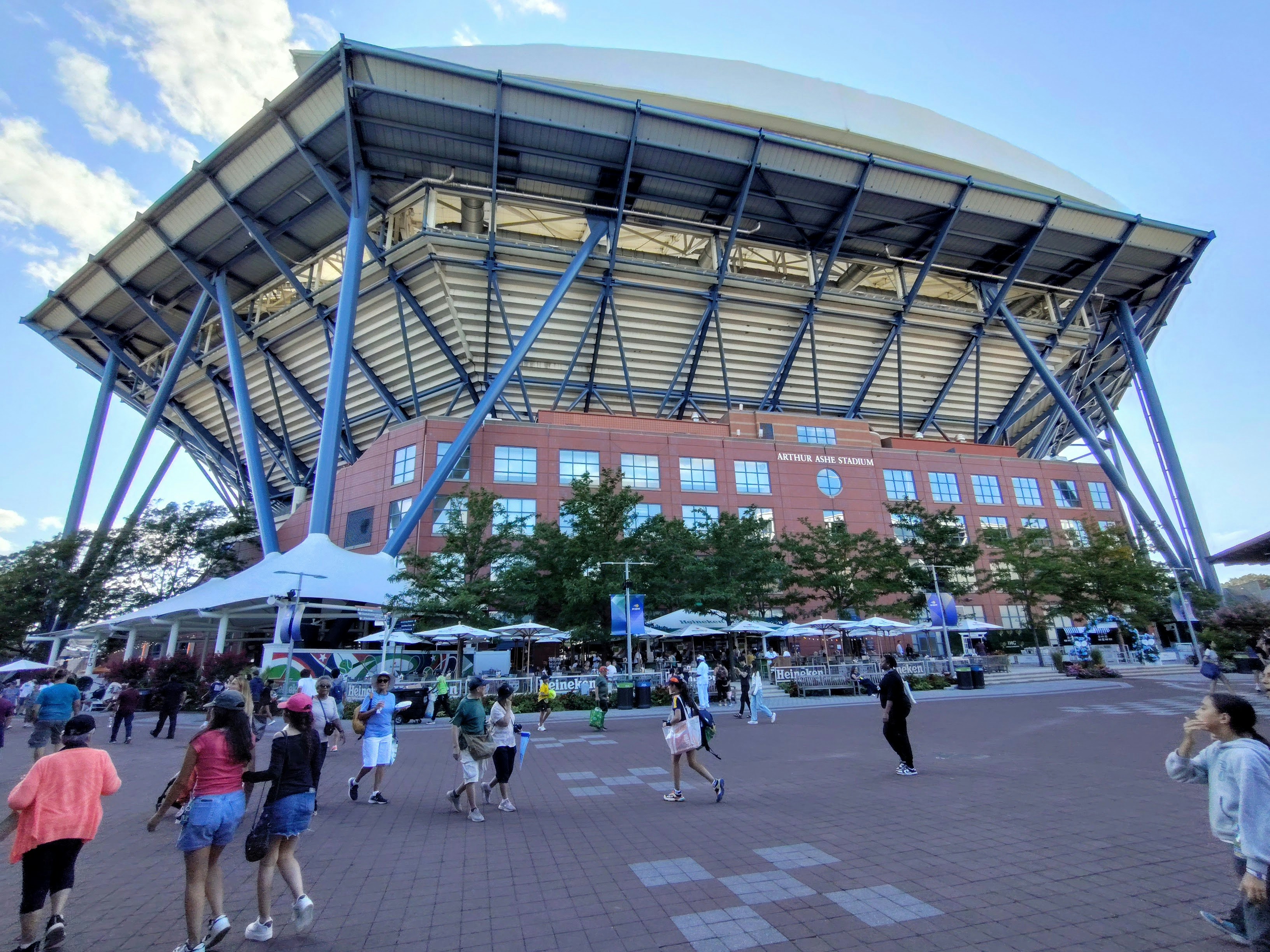 People walk outside a large stadium with a unique roof.