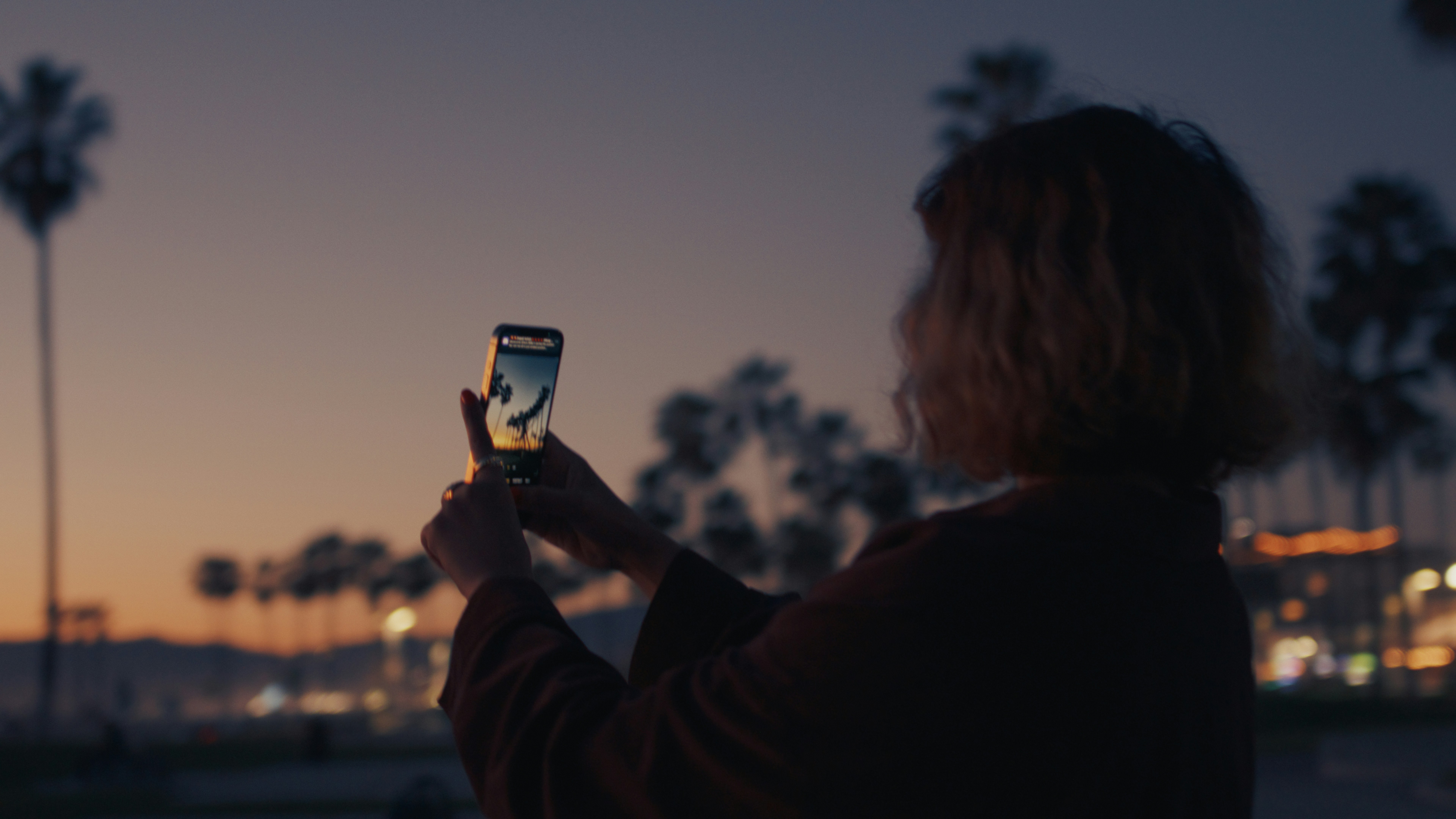 夕暮れ時にスマホで写真を撮る女性。