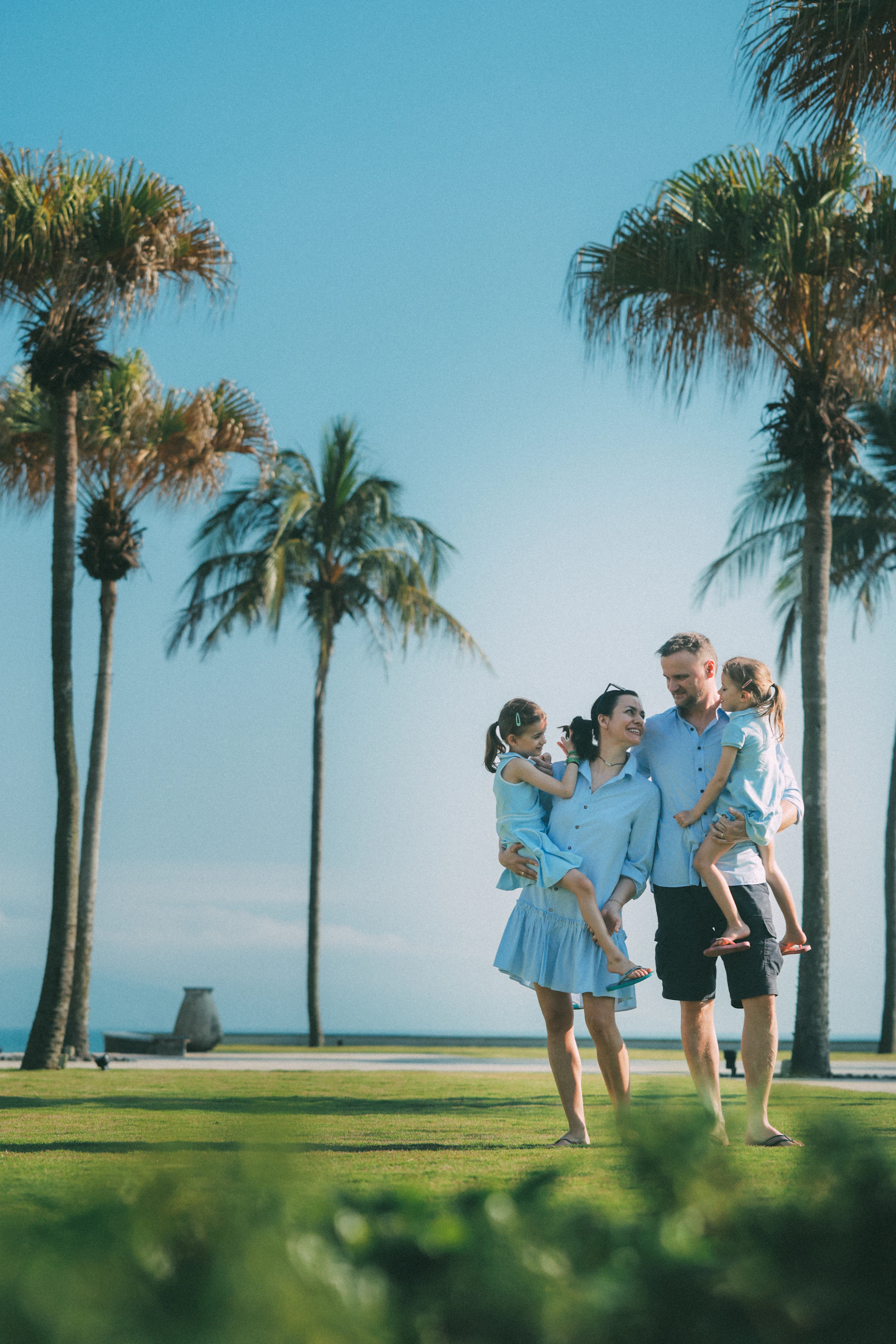 Family posing happily on a sunny day with palm trees.