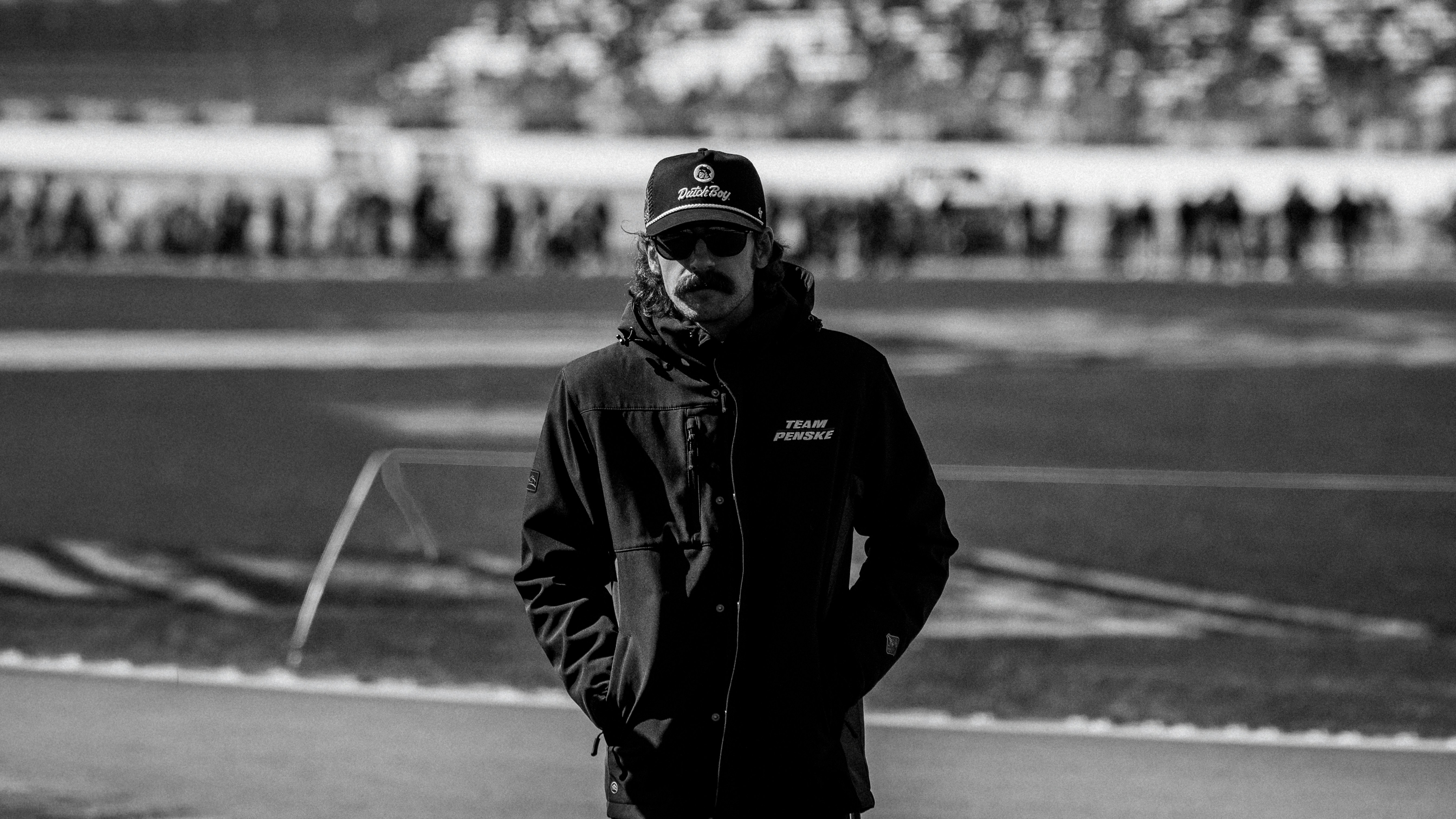Man in a hat and jacket standing on a field.