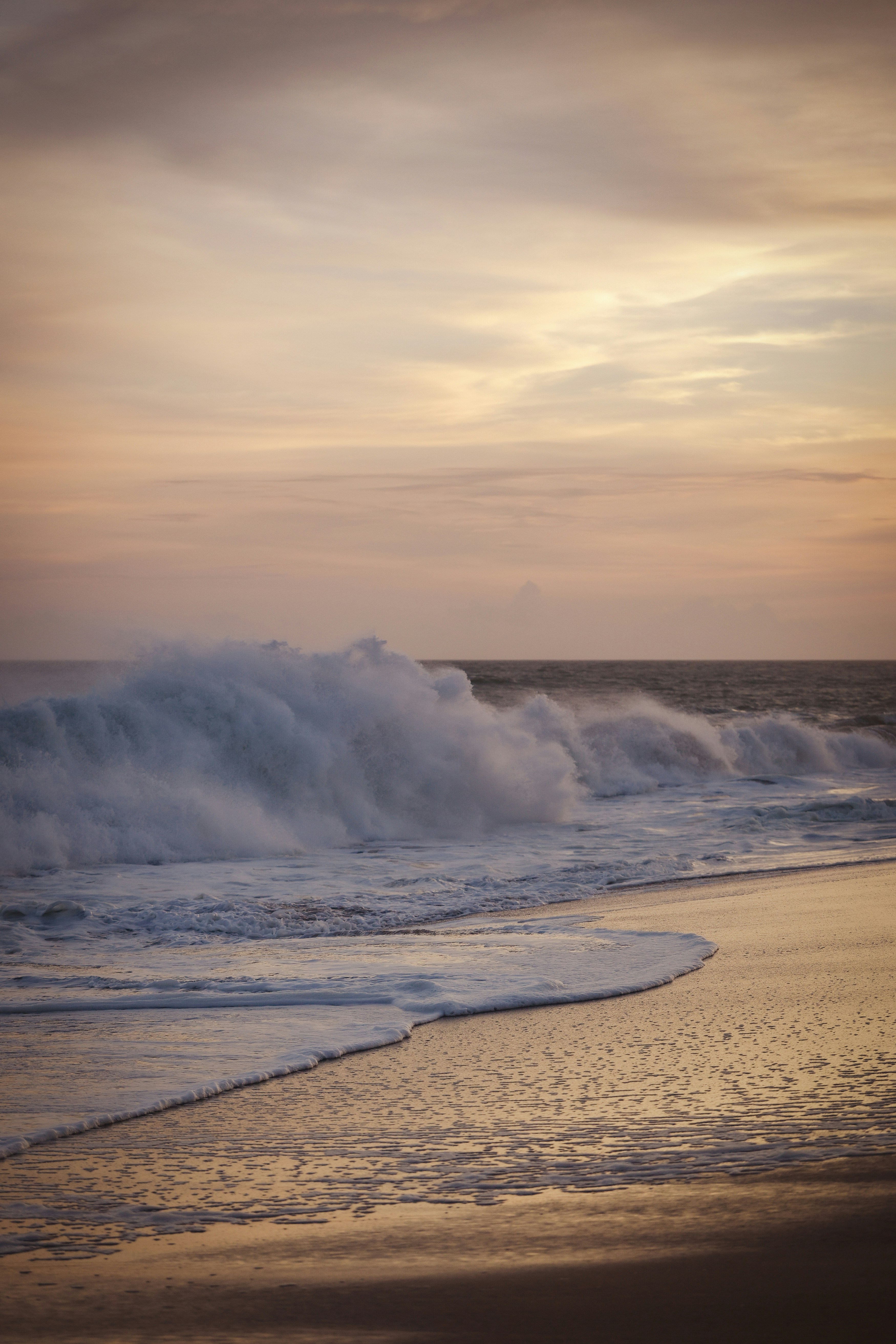 Ondas do oceano quebrando em uma praia de areia ao pôr do sol.