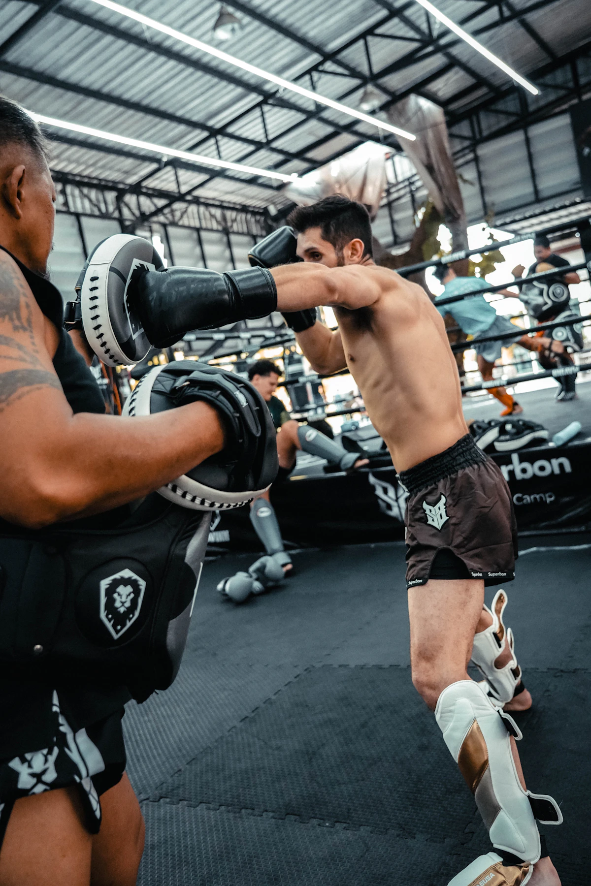 Two men training in a boxing ring, one holding Thai pads