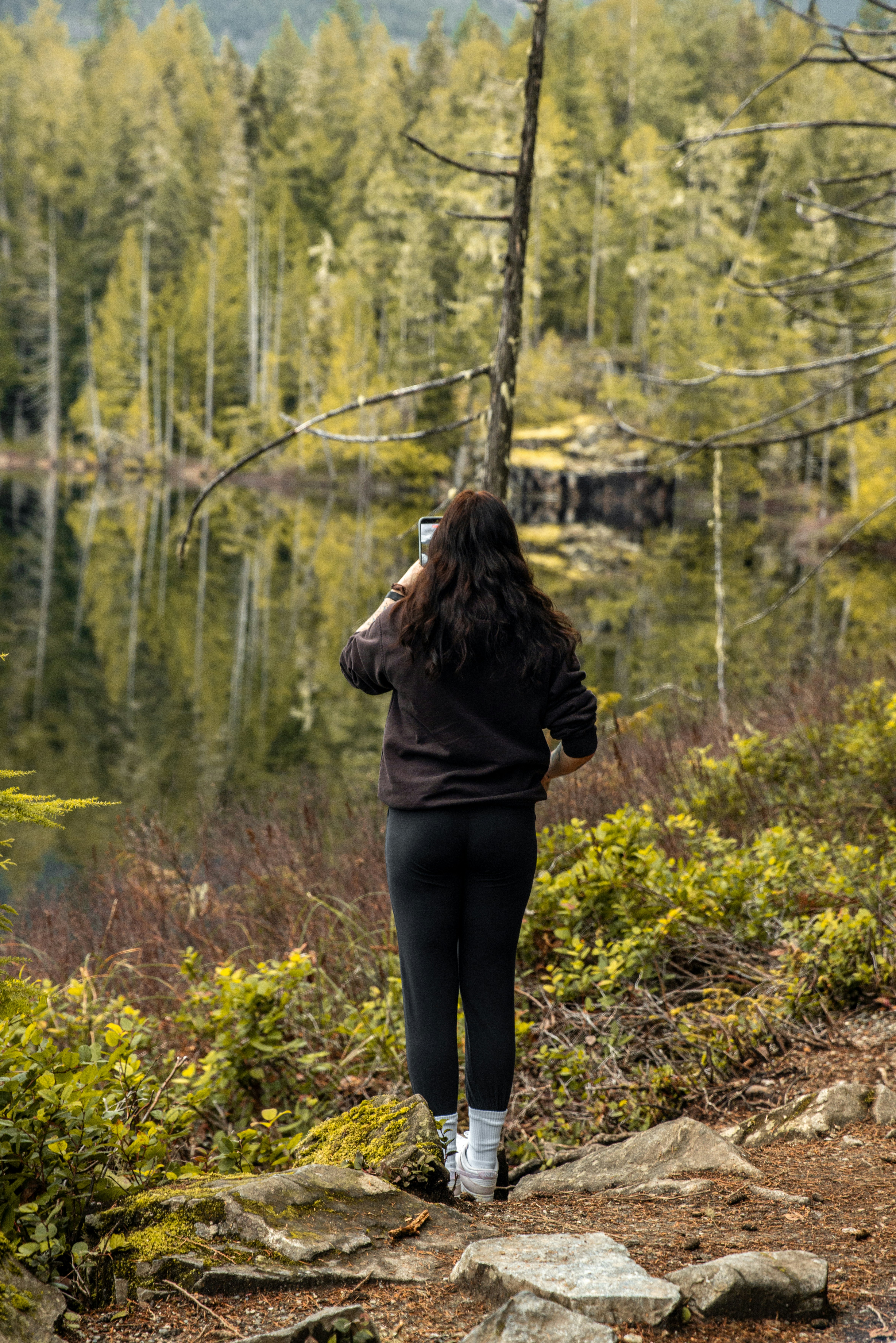 Frau, die ein Foto an einem reflektierenden Waldsee macht