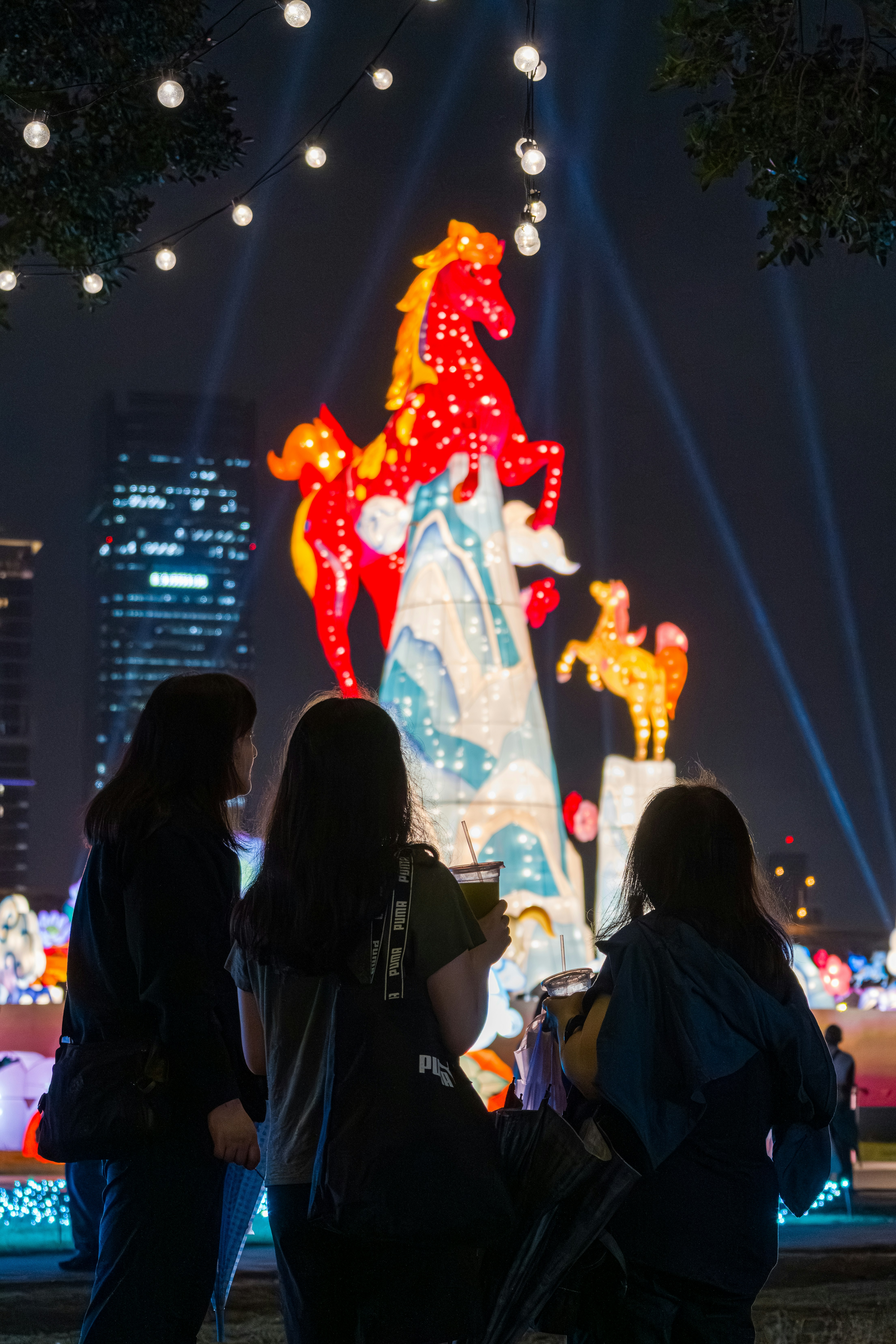 People admire large illuminated horse lanterns at night.