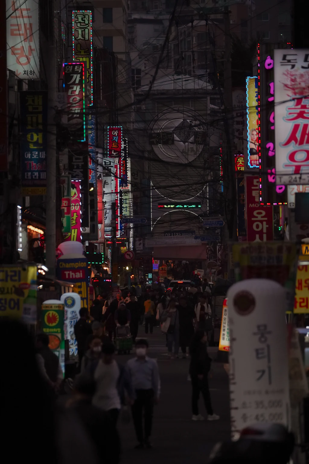 A crowded Seoul alley at night beneath stacked neon signs and dense overhead cables