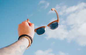Hand holding sunglasses against a bright blue sky