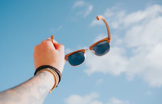 Hand holding sunglasses against a bright blue sky