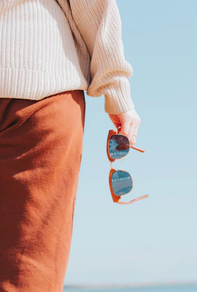 Person holding sunglasses against a clear blue sky