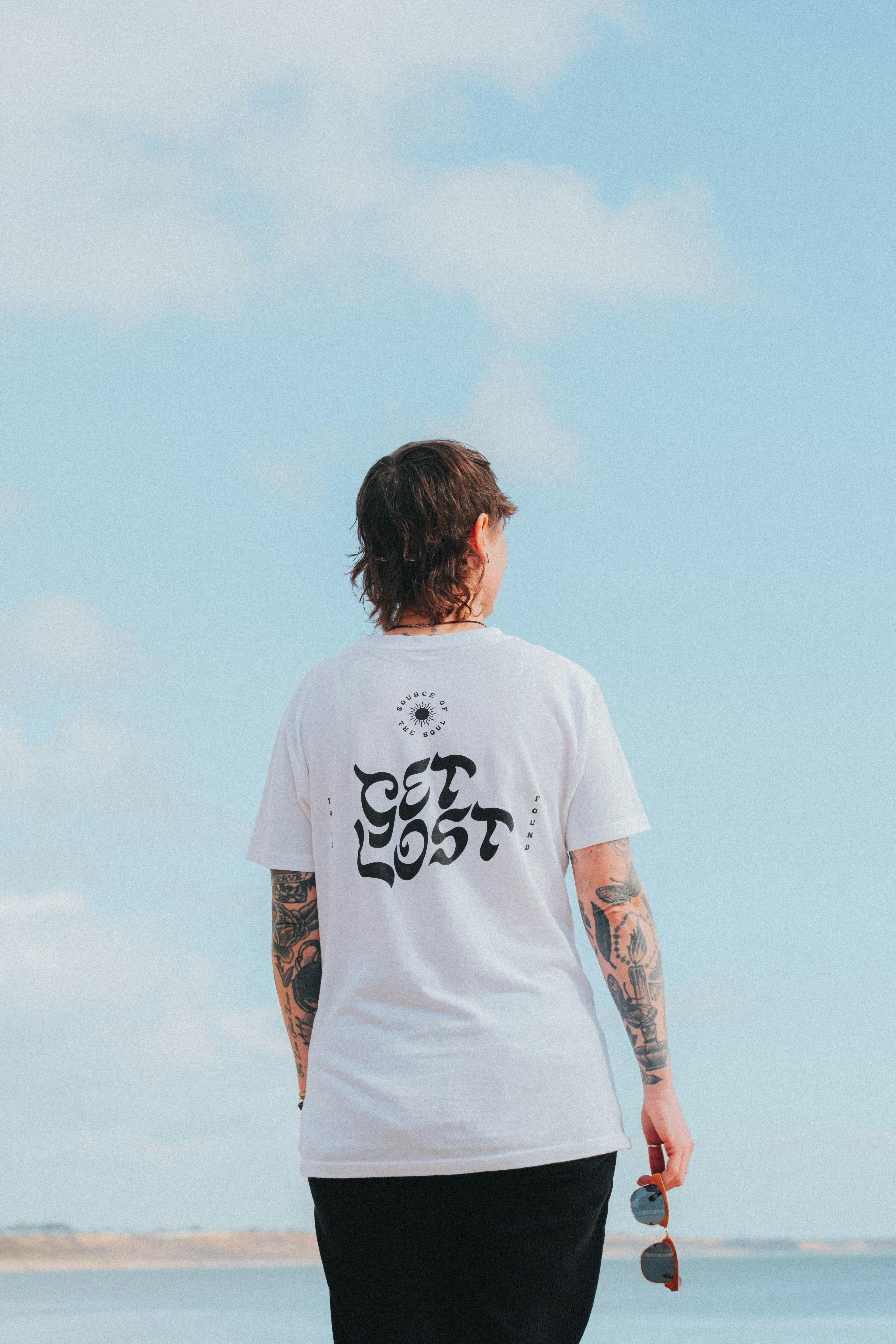 Person with tattoos wearing a white t-shirt with text.