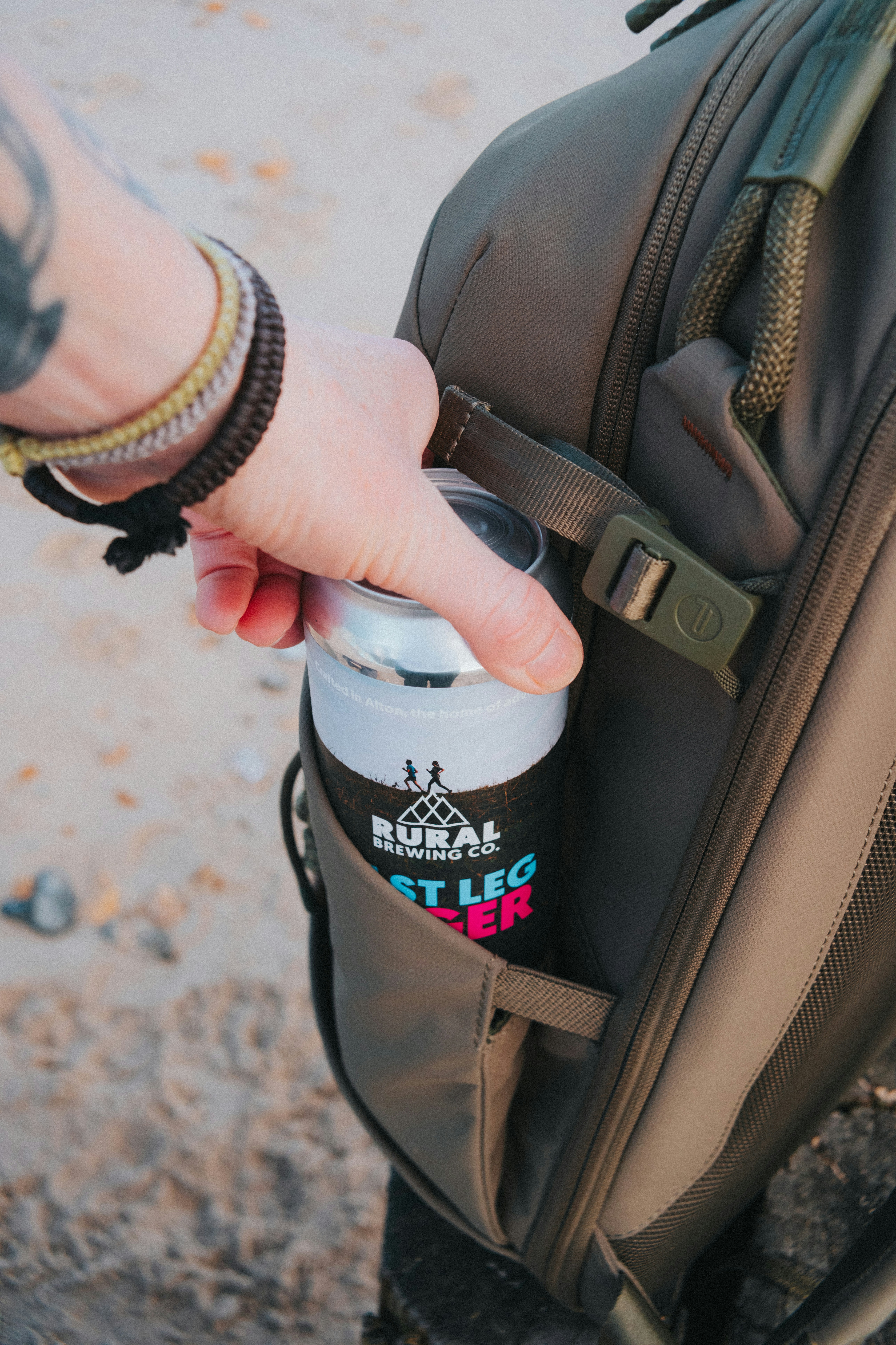 Hand placing a beer can into a backpack pocket.
