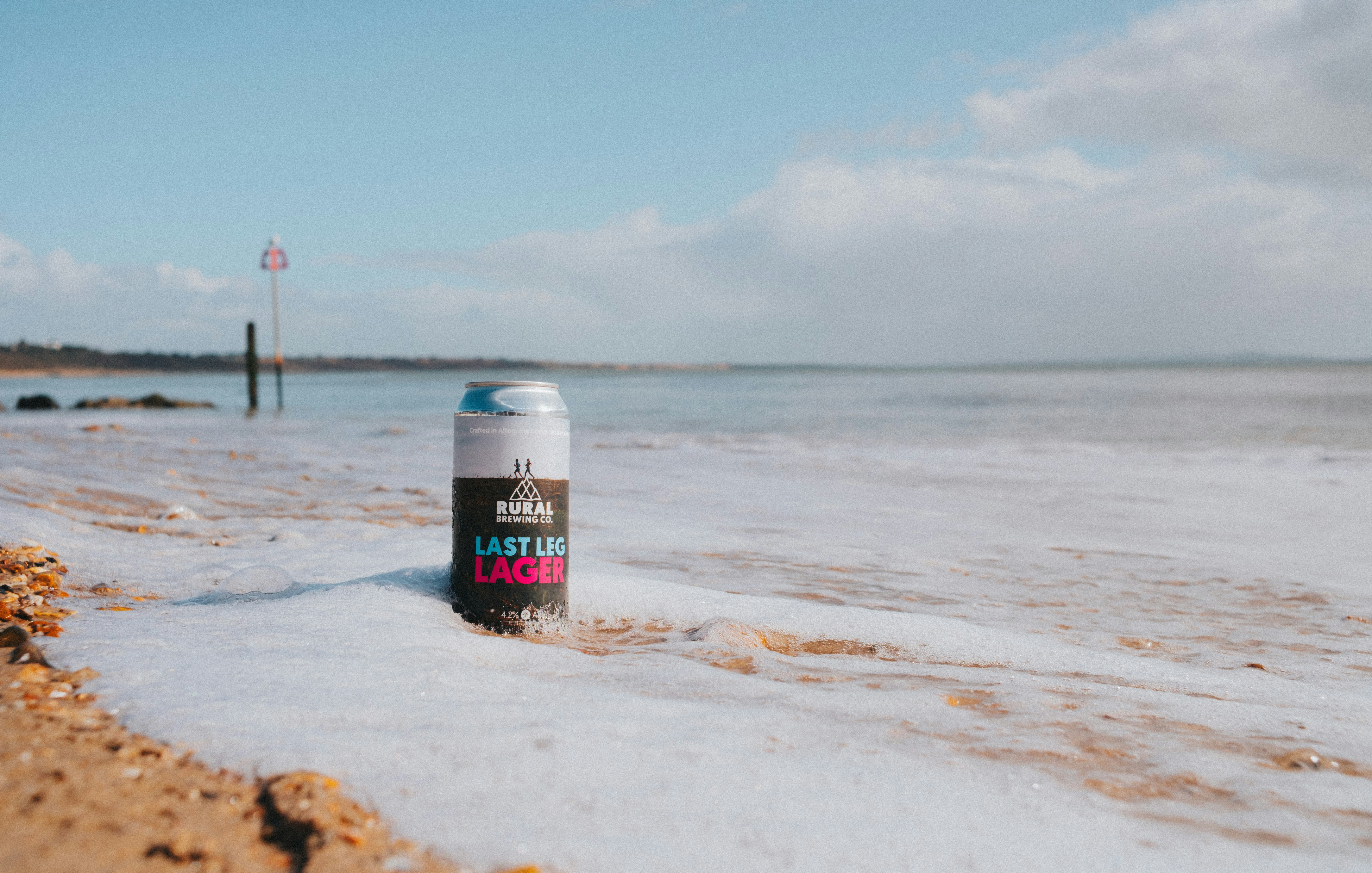 A can of beer sits on a foamy beach.