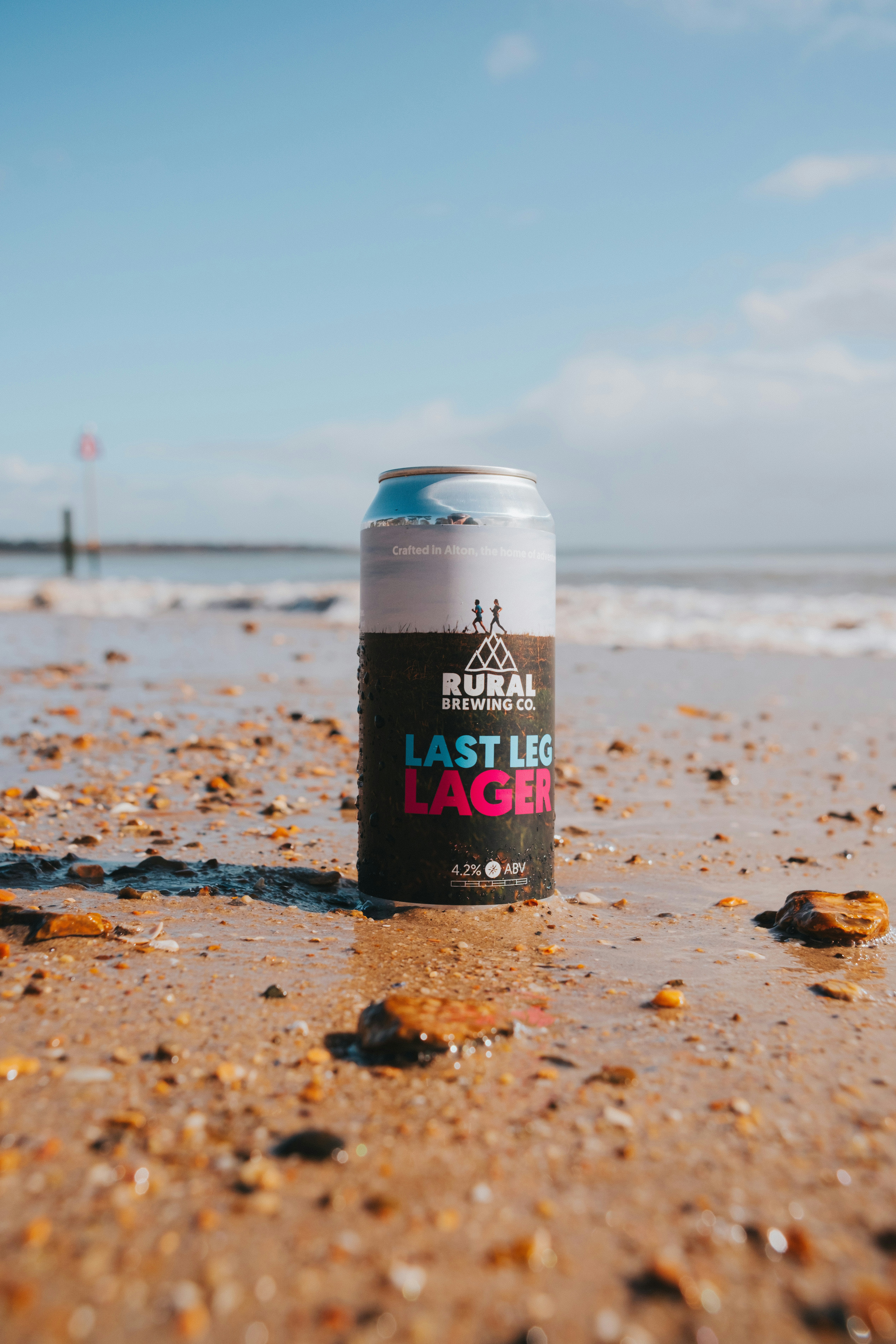 A can of lager sits on a sandy beach.
