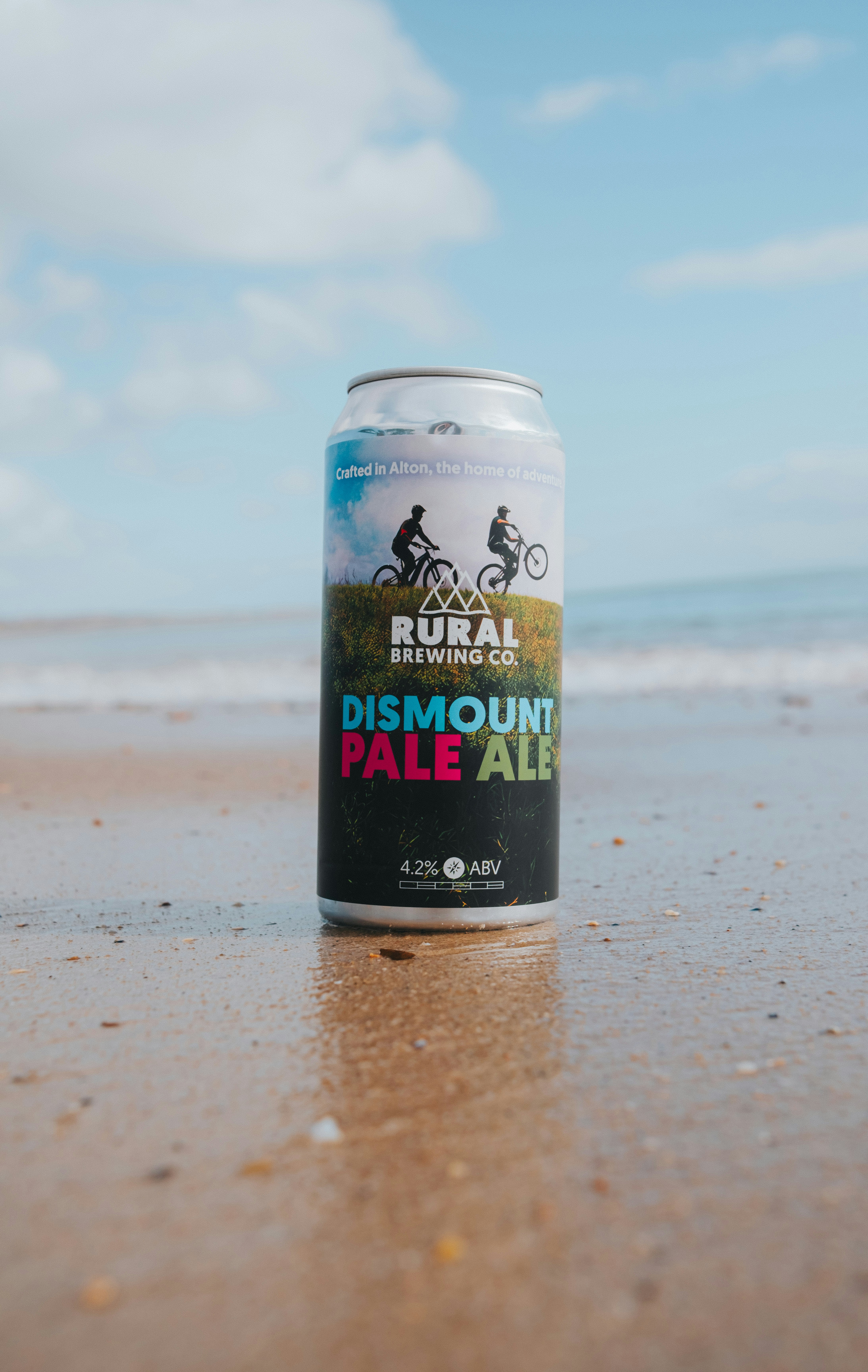 A can of dismount pale ale on a sandy beach.