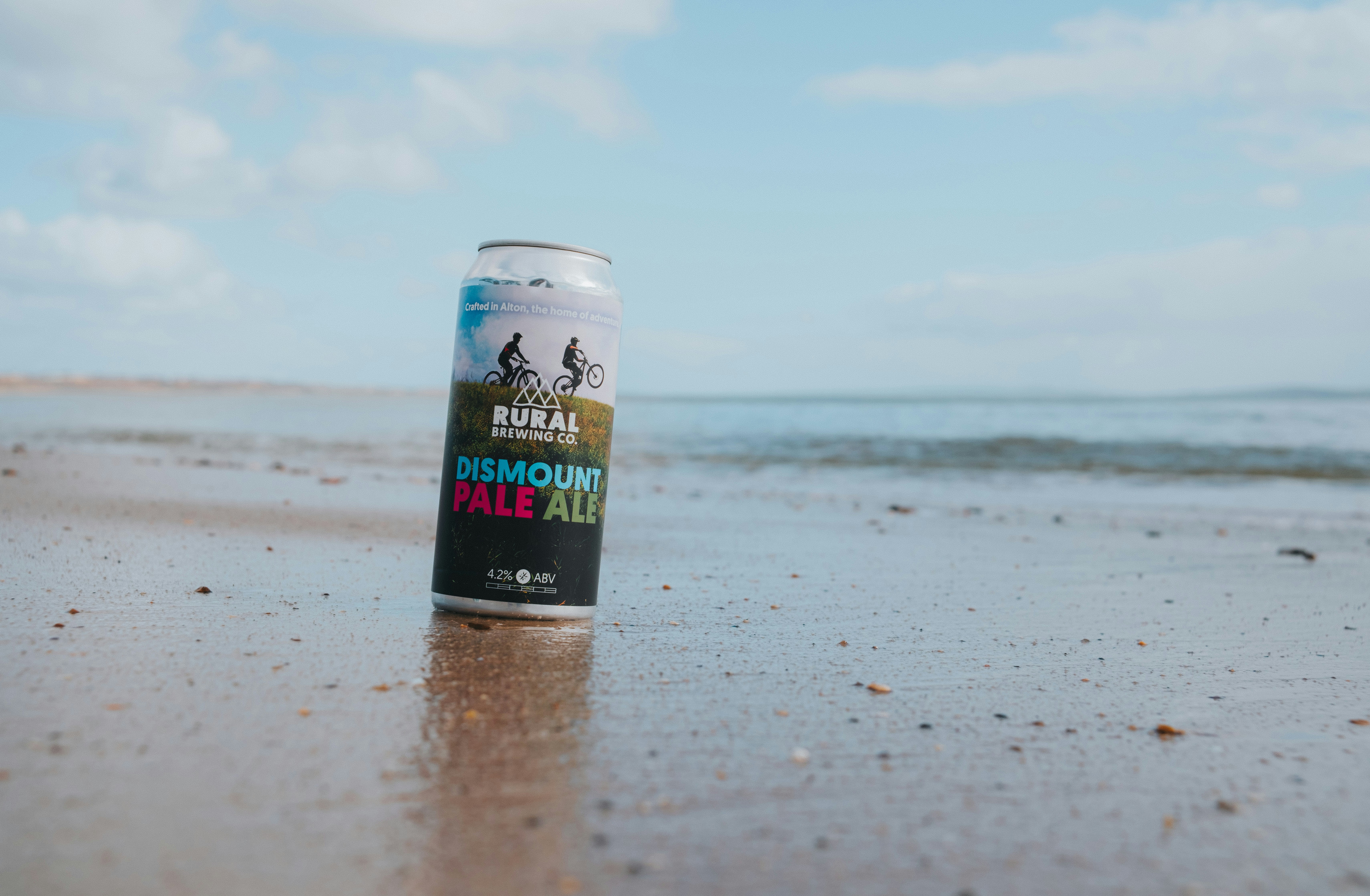 A can of beer sits on a sandy beach.