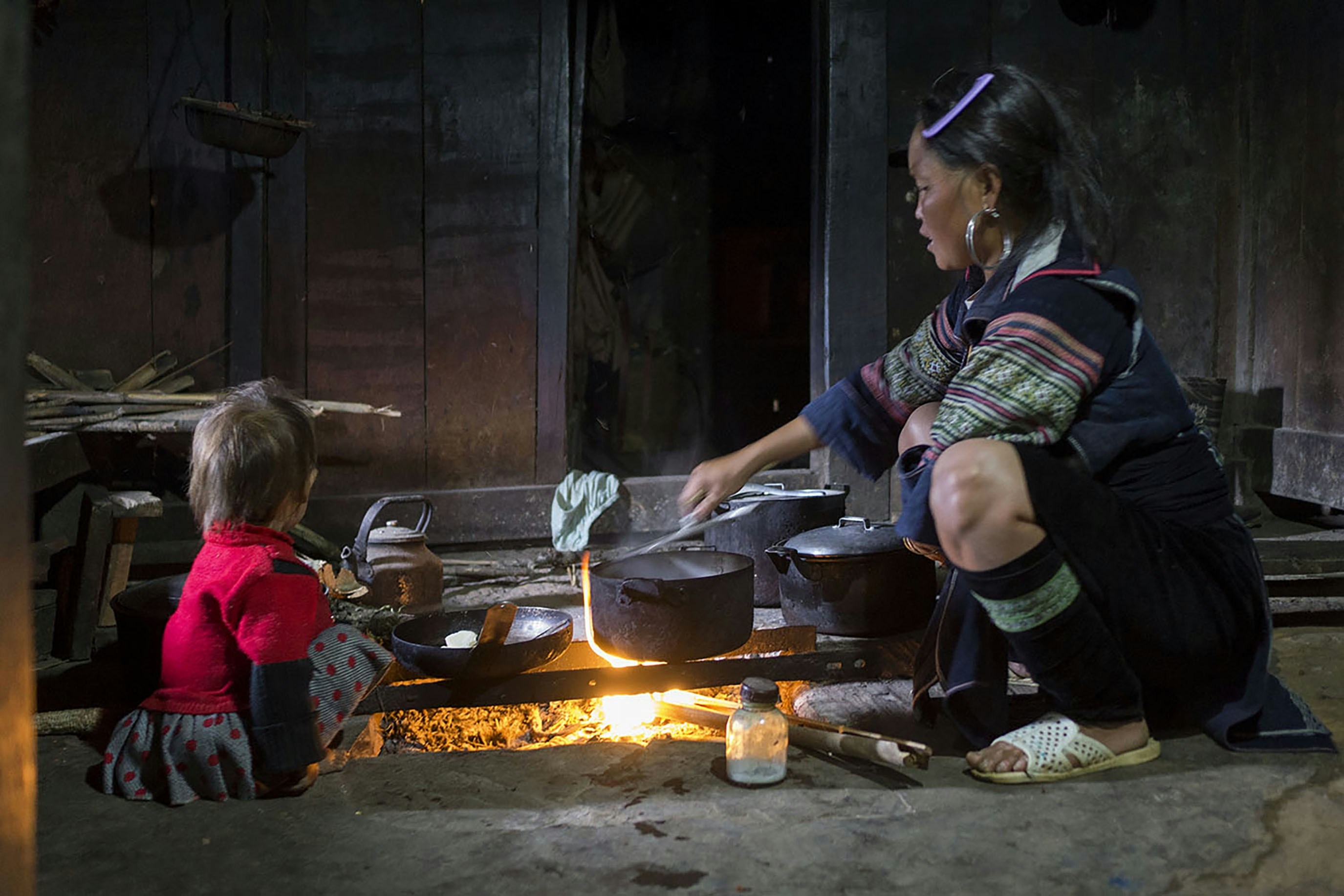 아이가 지켜보는 가운데 불 앞에서 요리하는 여성