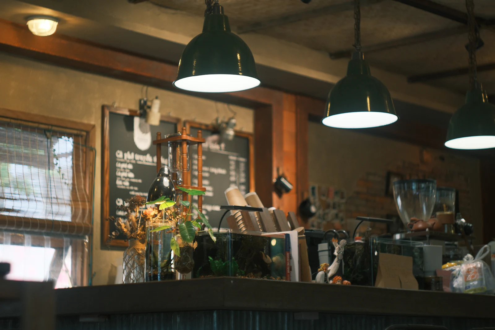 A cafe interior under two enamel pendant lamps, chalkboard menu behind the counter.